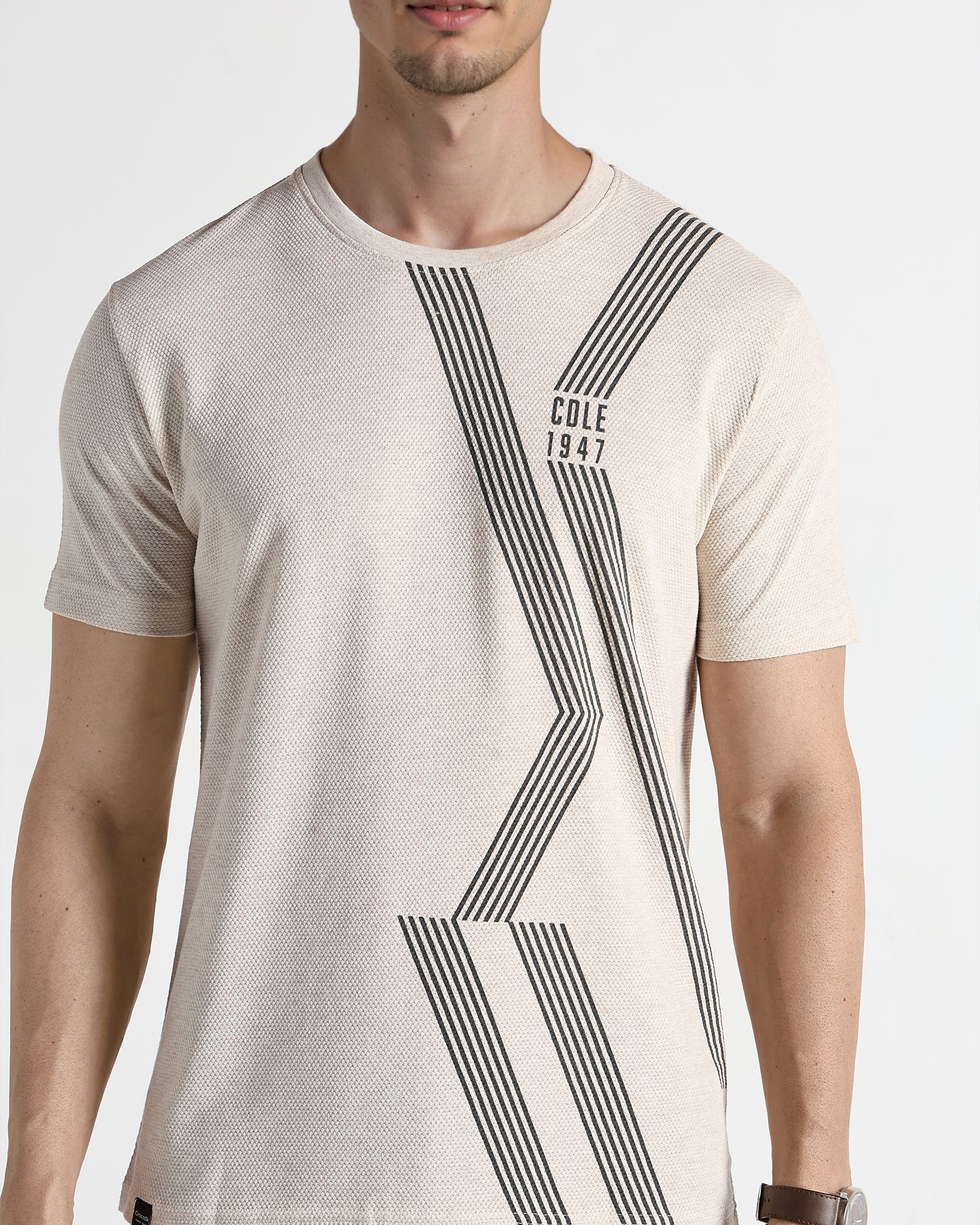 Man wearing a beige t-shirt with black geometric design on a white background