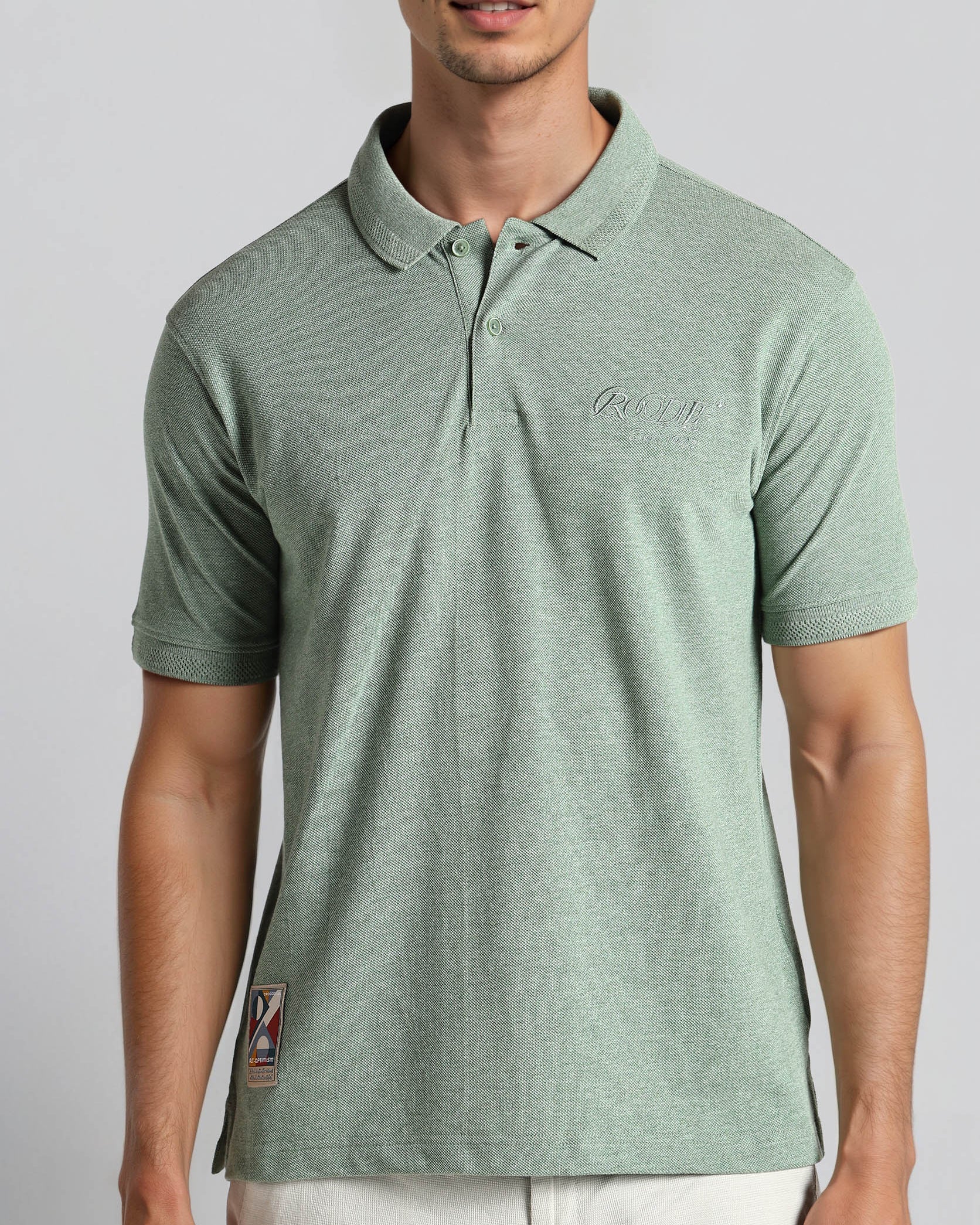 Man wearing a green polo shirt with a logo on a plain background