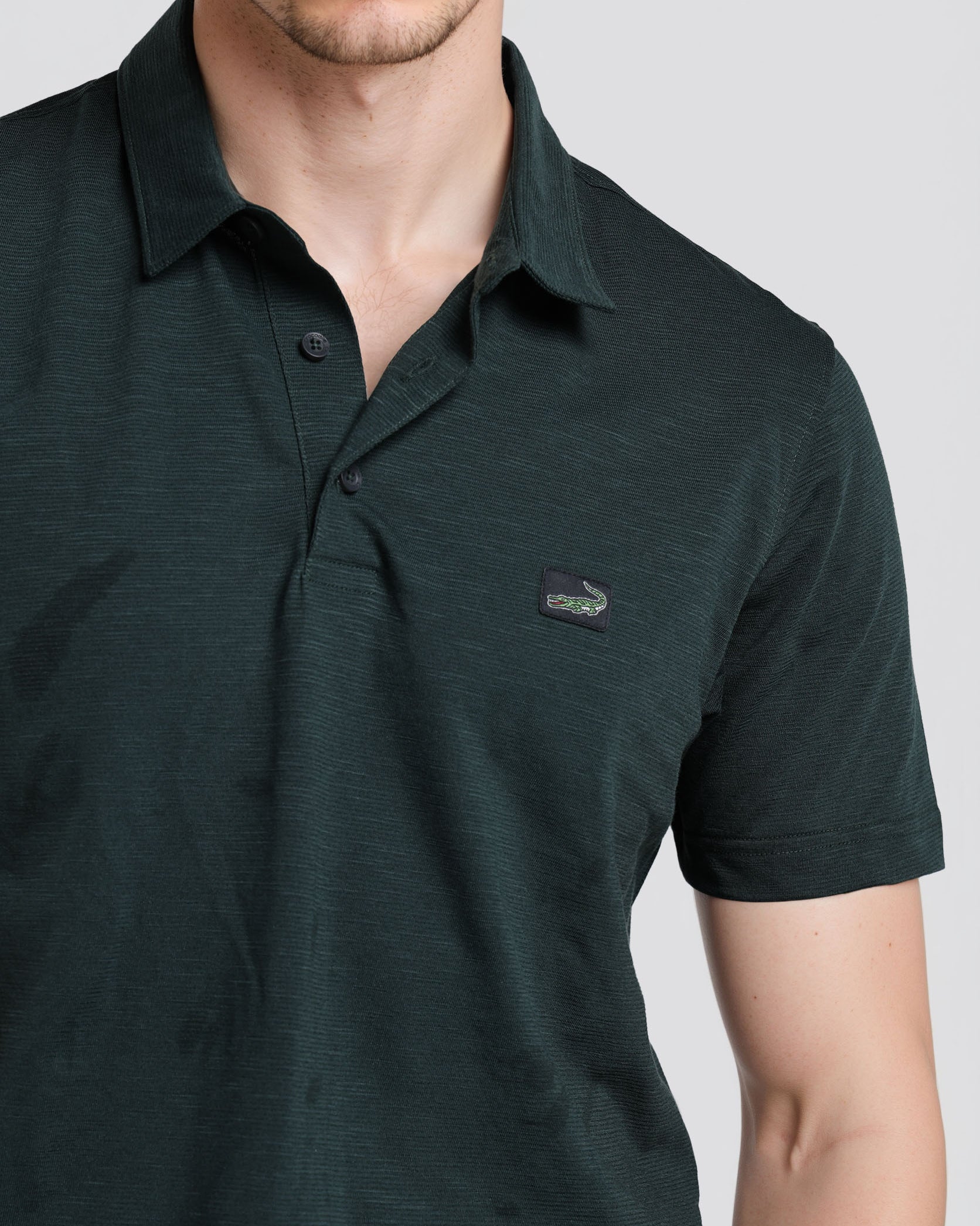 Man wearing a dark green polo shirt with a small logo on a light gray background