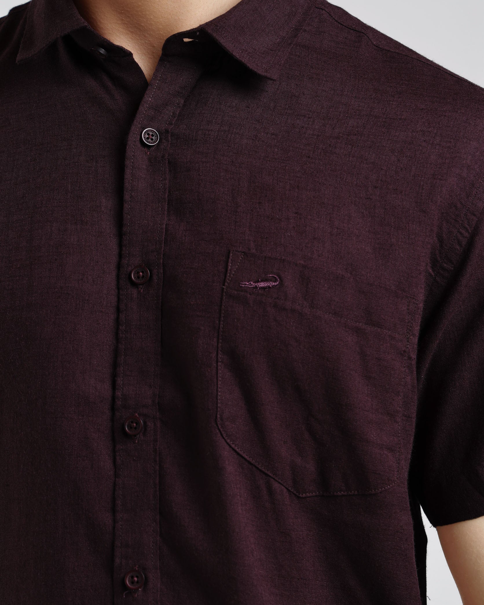 Close-up of a maroon button-up shirt with a pocket on a plain background