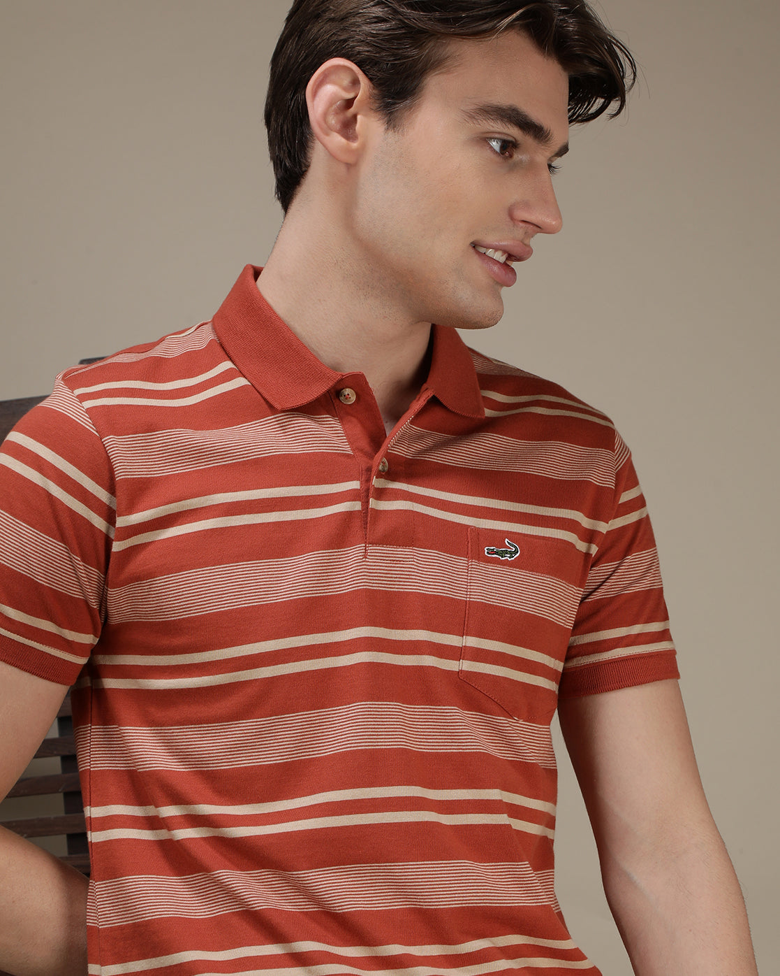 Man wearing a dusty orange striped polo t shirt with casual styling on a gray background