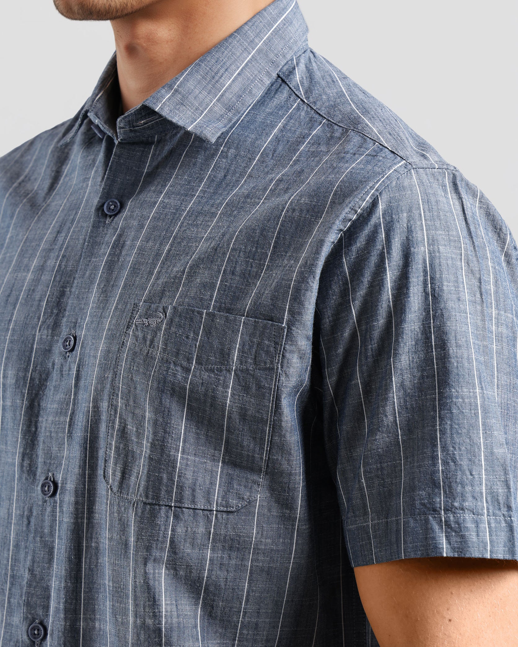Close-up of a person wearing a blue striped shirt with a pocket on a gray background