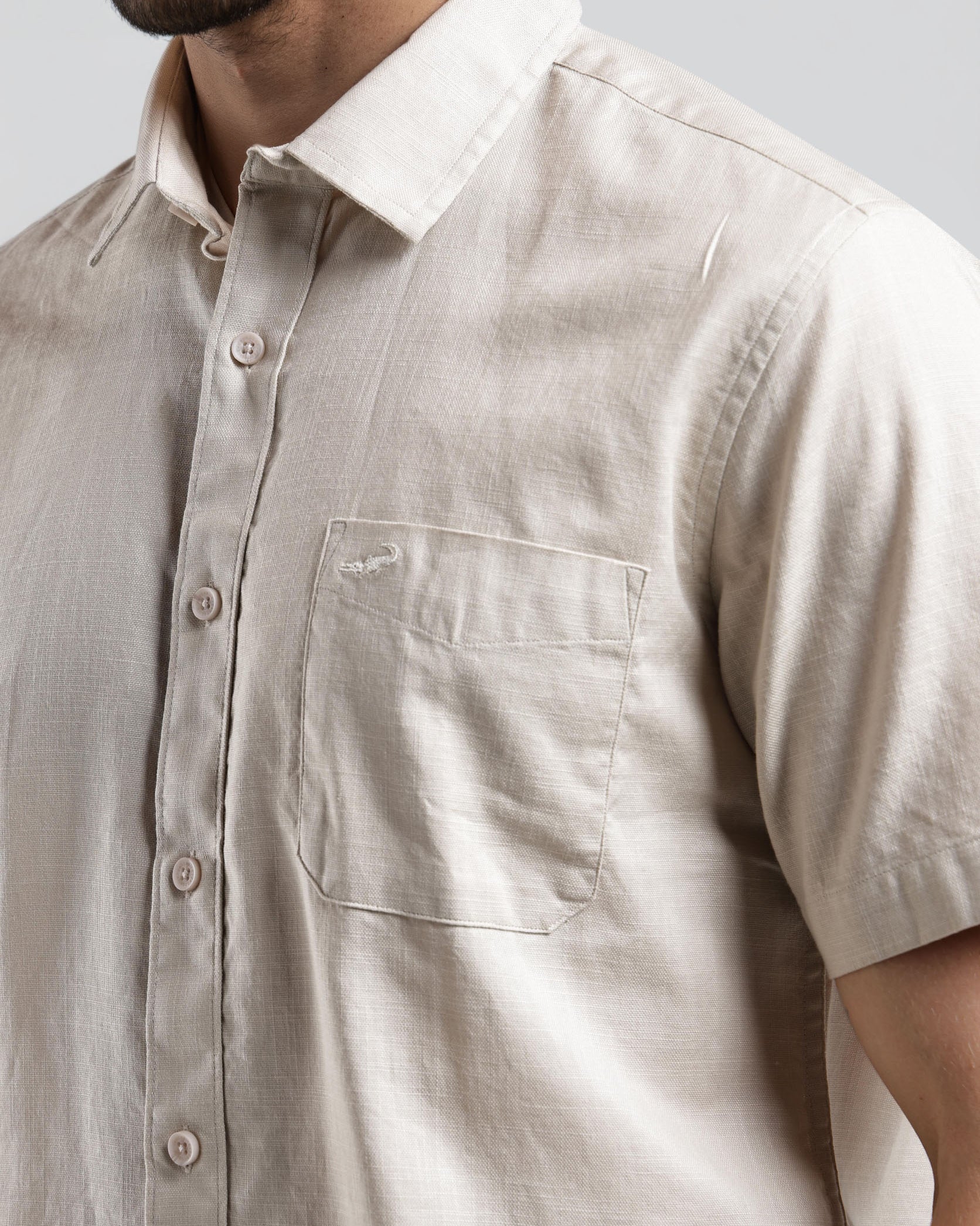 Beige short-sleeve shirt worn by a person on a plain background