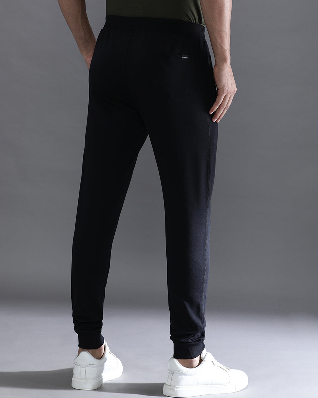 Person wearing black jogger pants and white sneakers on a gray background