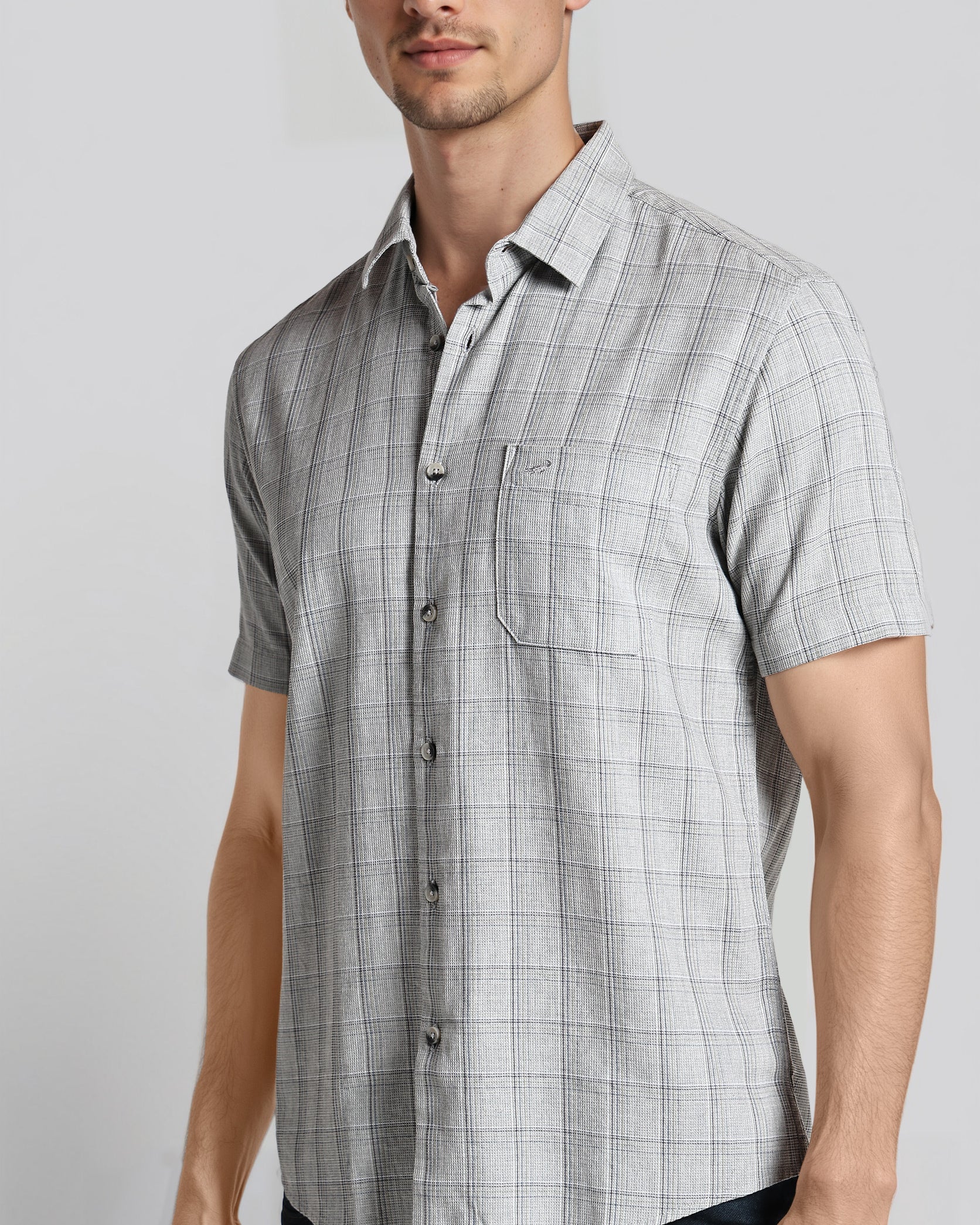 Man wearing a gray checkered short-sleeve shirt against a plain background
