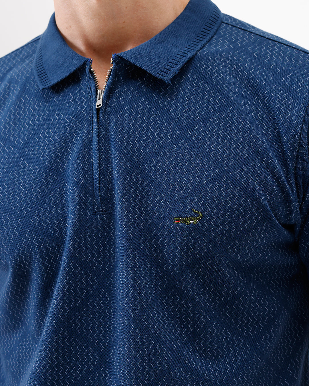 A man wearing a navy blue short-sleeve polo shirt with a subtle geometric pattern and a half-zip collar, paired with gray trousers, against a plain white background.