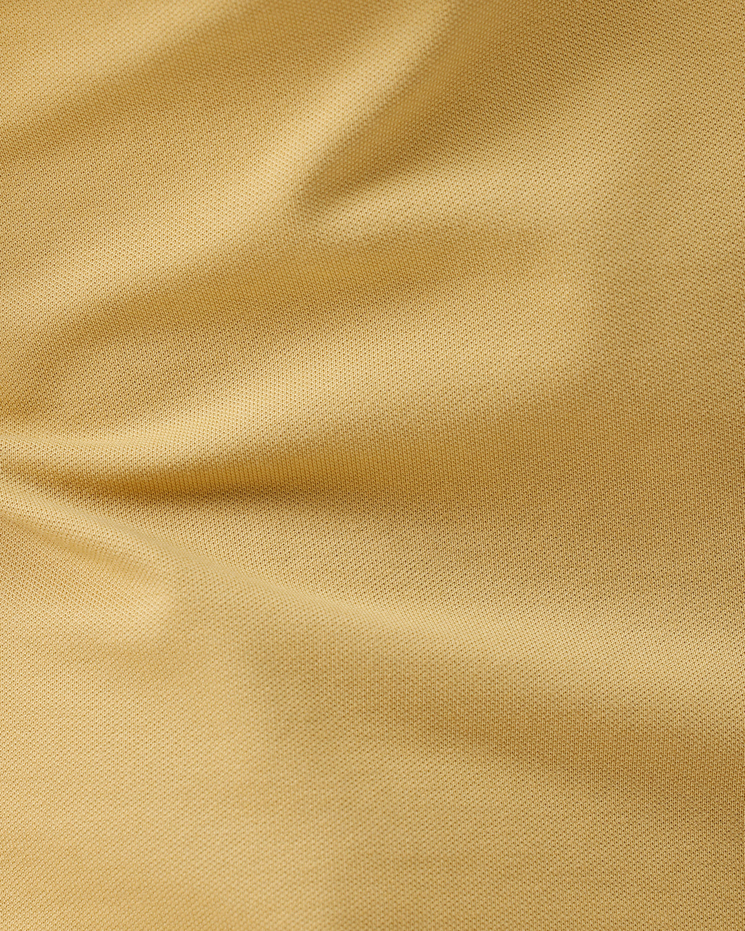 A man wearing a light yellow Lacoste polo shirt with dark piping on the collar and sleeve cuffs, paired with beige trousers, against a plain white studio background.