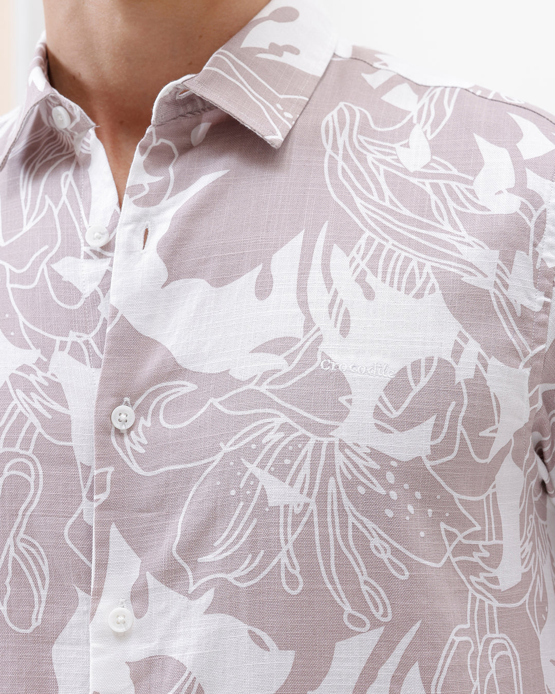 A man wearing a long-sleeve button-up shirt with a light gray and white abstract floral pattern, paired with dark blue jeans, standing against a plain white background.