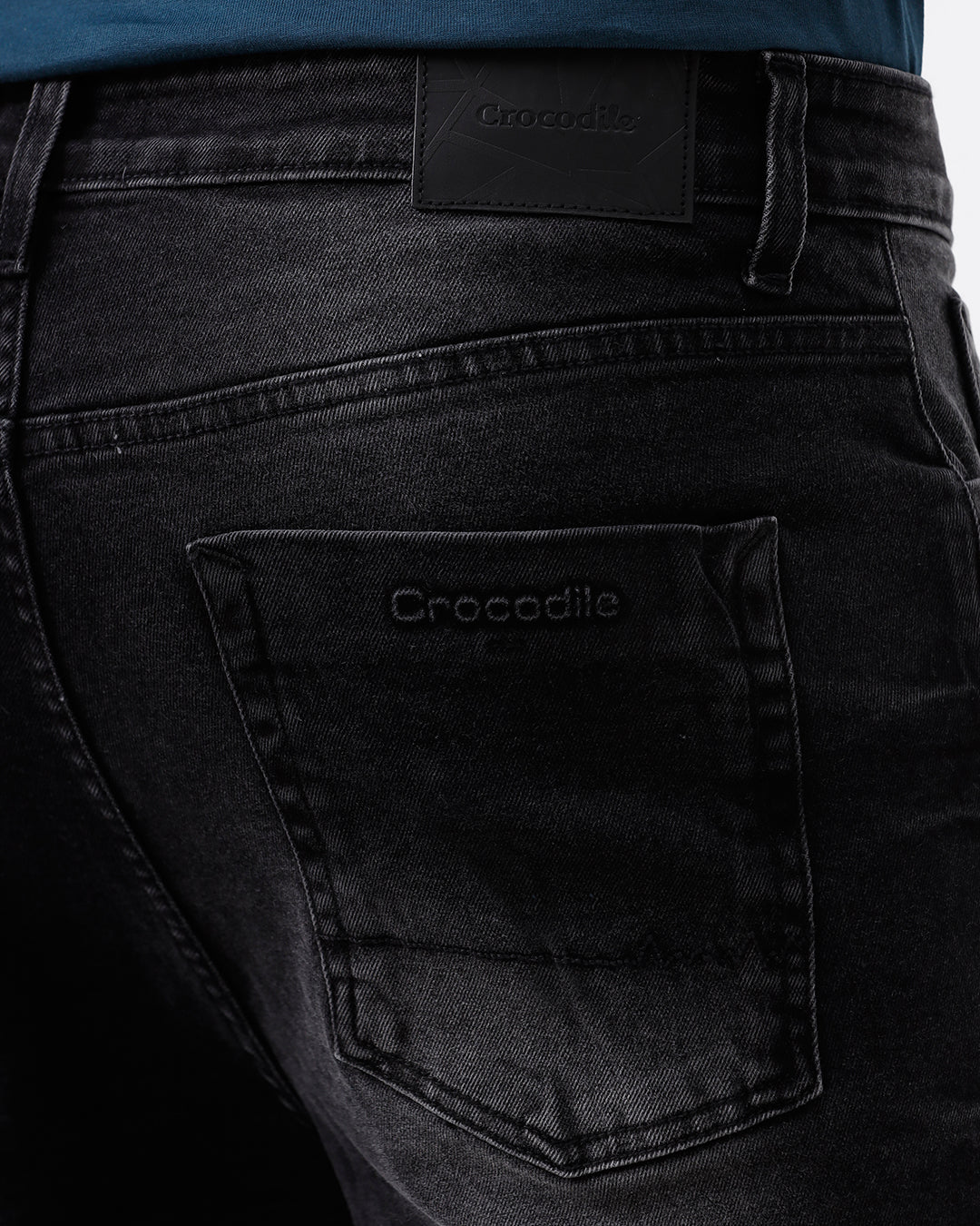 A person wearing slim-fit black denim jeans with a faded wash, paired with a dark blue t-shirt and black leather boots, shown from the waist down on a light gray studio background.
