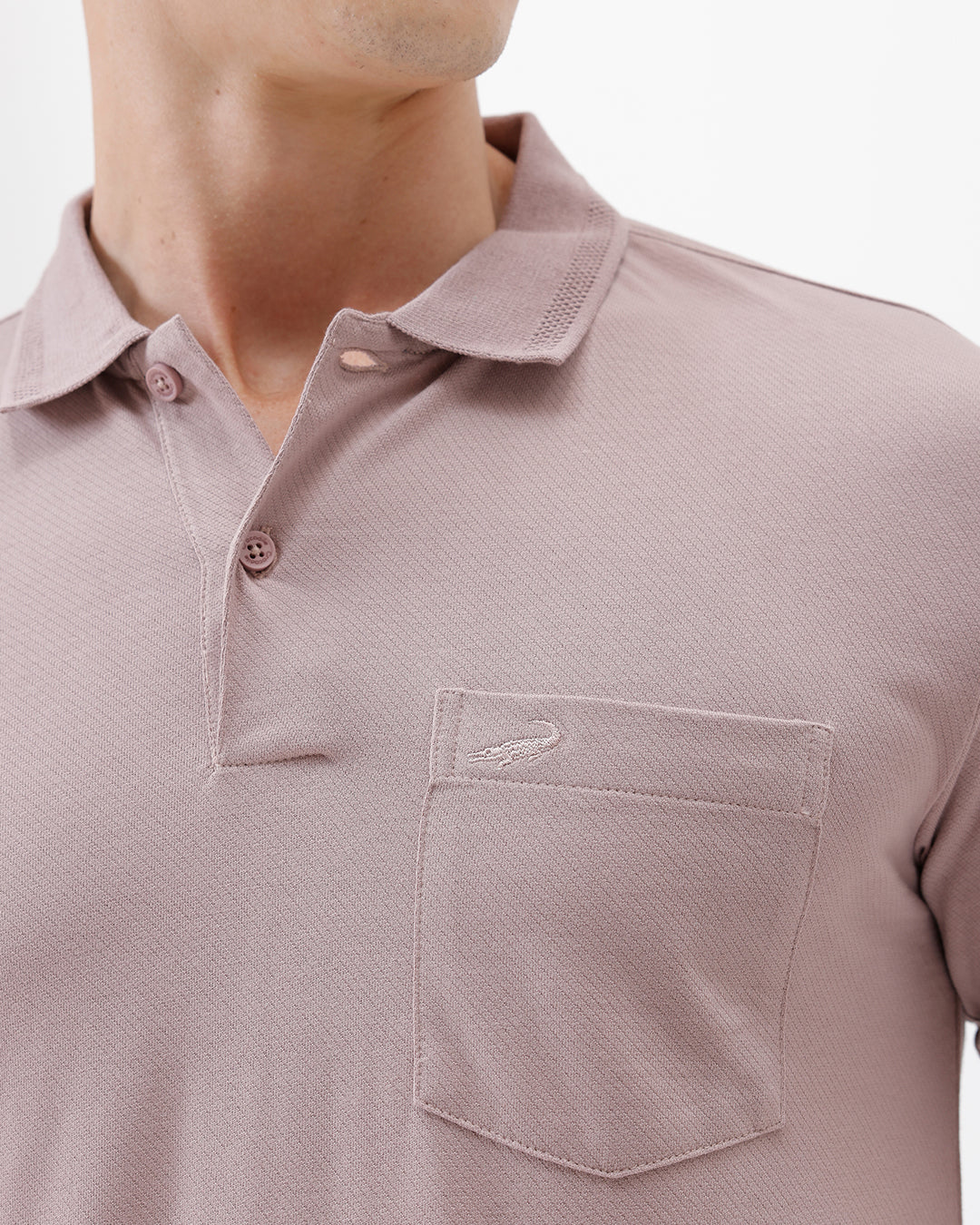 A man modeling a short-sleeve polo shirt in a dusty mauve-pink color, paired with khaki cargo pants and a baseball cap, against a plain light gray background.