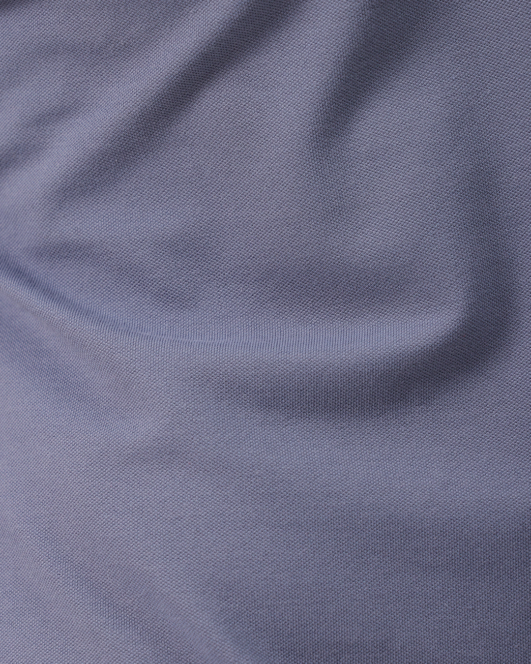 A man wearing a slate blue polo shirt and beige trousers, standing against a plain white background.