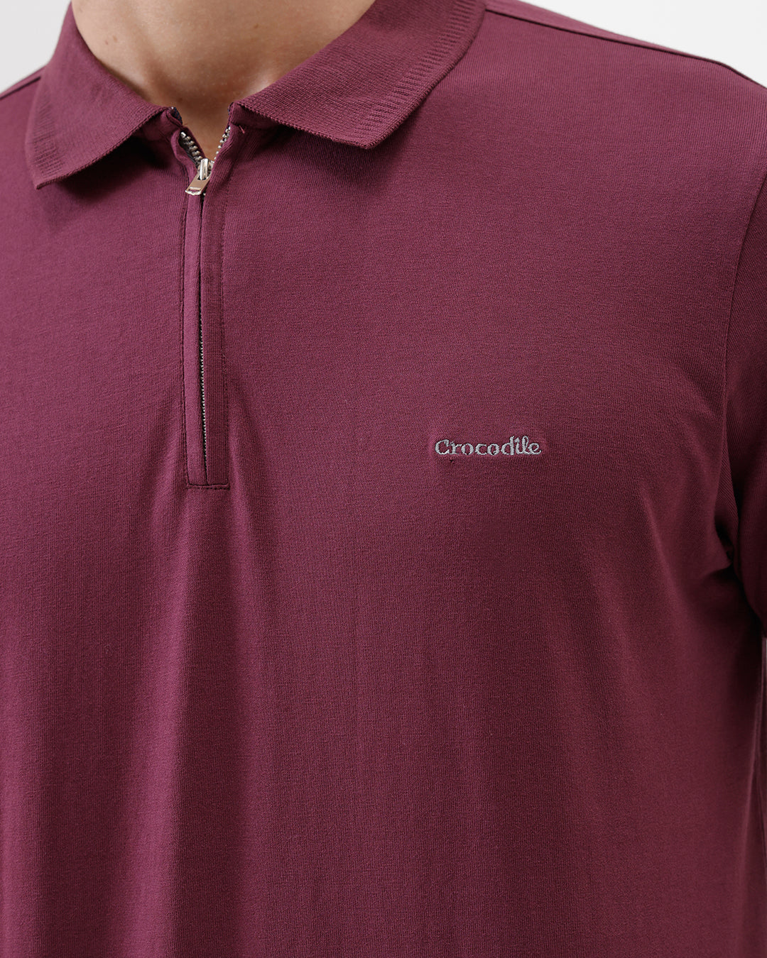 A man wearing a short-sleeve polo shirt in maroon with gray sleeve trim and a half-zip collar, paired with beige cargo pants, against a plain white studio background.