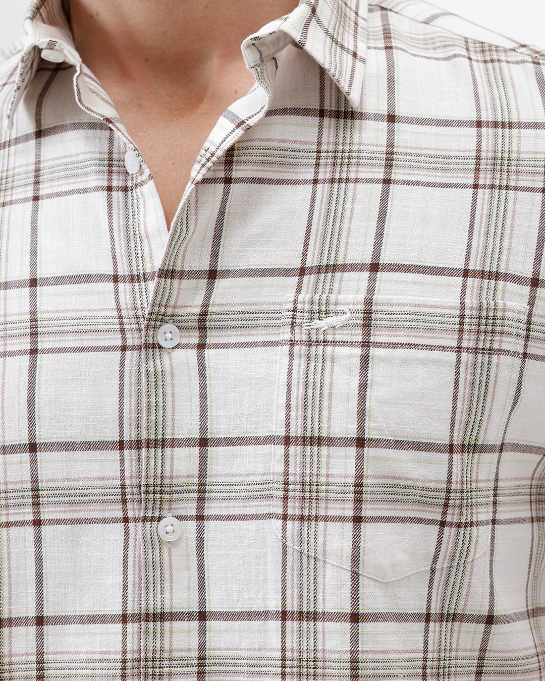 A man wearing a long-sleeve plaid button-up shirt in beige and brown with dark blue jeans, standing against a plain white studio background.