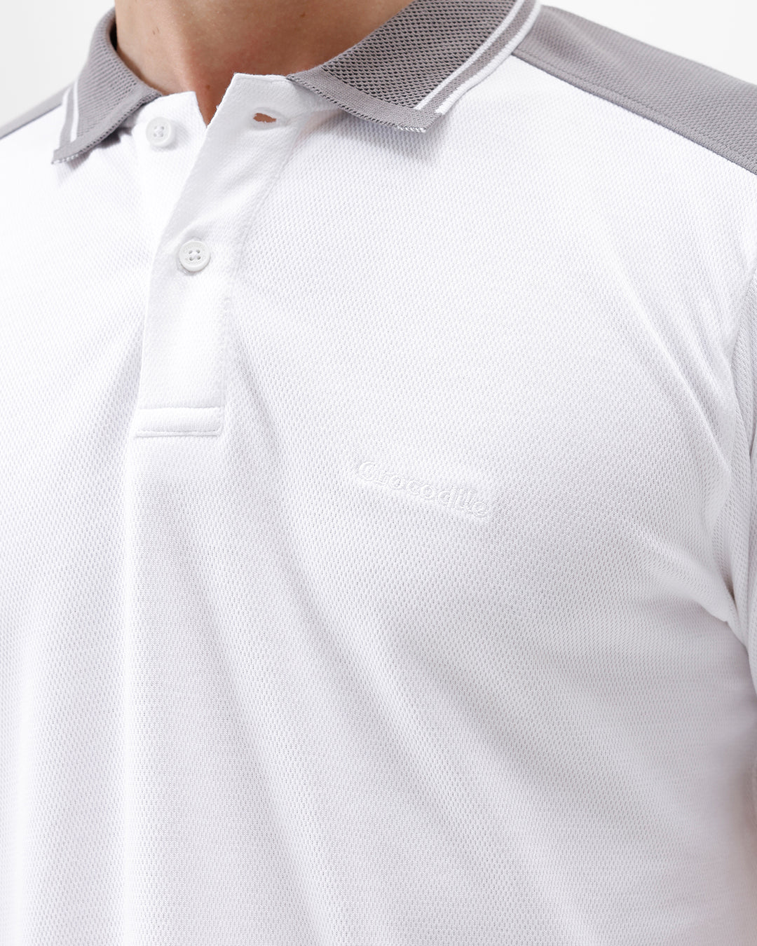 A man modeling a white short-sleeve polo shirt with gray shoulder panels and gray striped trim on the sleeves, paired with gray trousers and black sunglasses, against a plain white background.