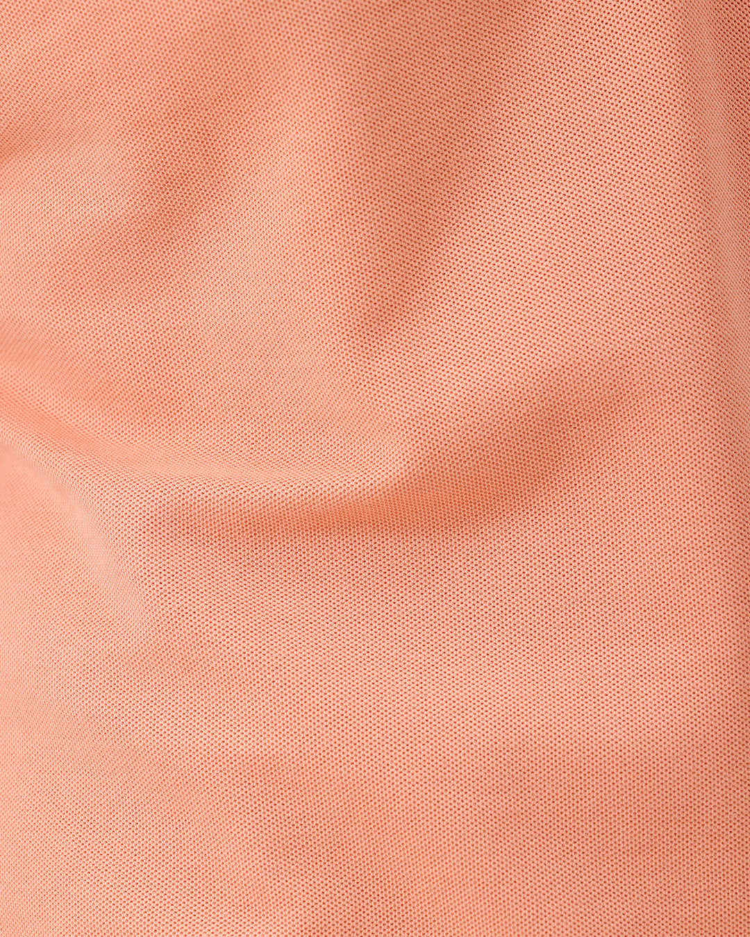 A man wearing a peach-colored short-sleeve polo shirt and beige trousers, standing against a plain white studio background.