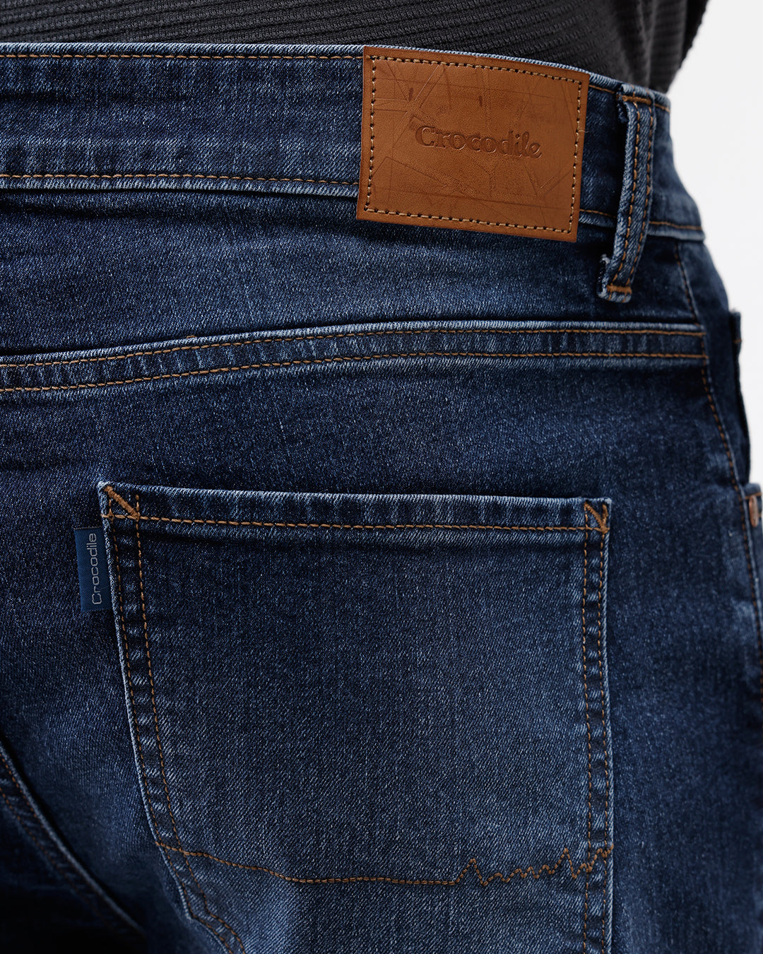 A person wearing dark blue slim-fit jeans with a faded wash, paired with a black t-shirt and white sneakers, shown from the waist down against a plain white studio background.
