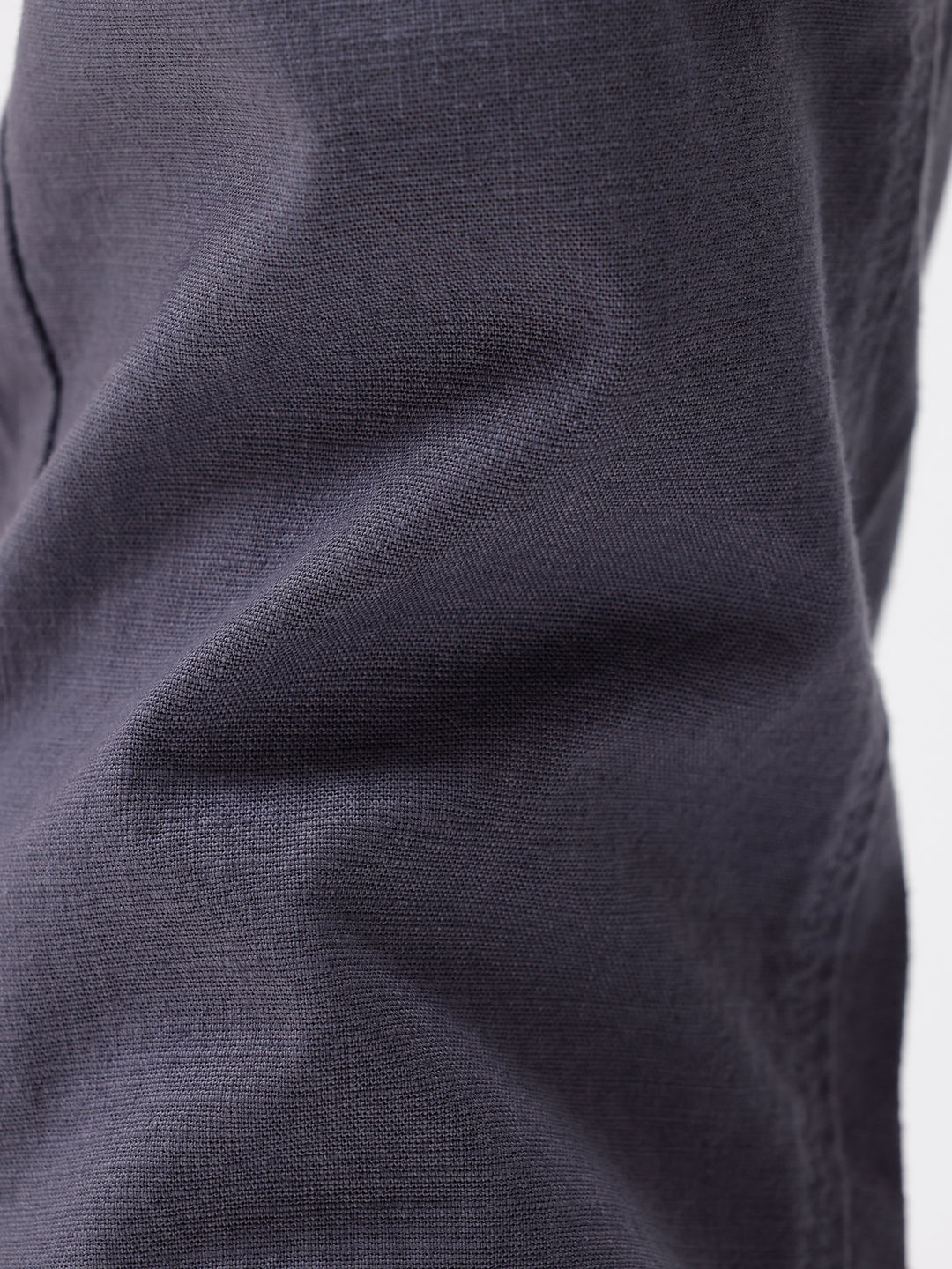 A person wearing slim-fit charcoal gray chino pants, paired with a dark purple shirt and white sneakers, standing against a plain white studio background.