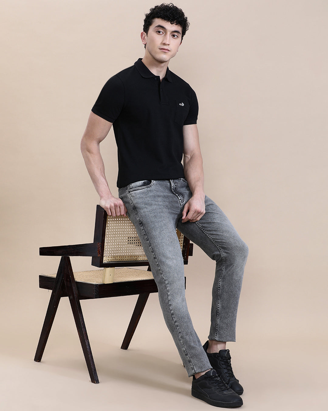 Man wearing a black casual solid black polo t shirt with pocket with casual styling on a gray background