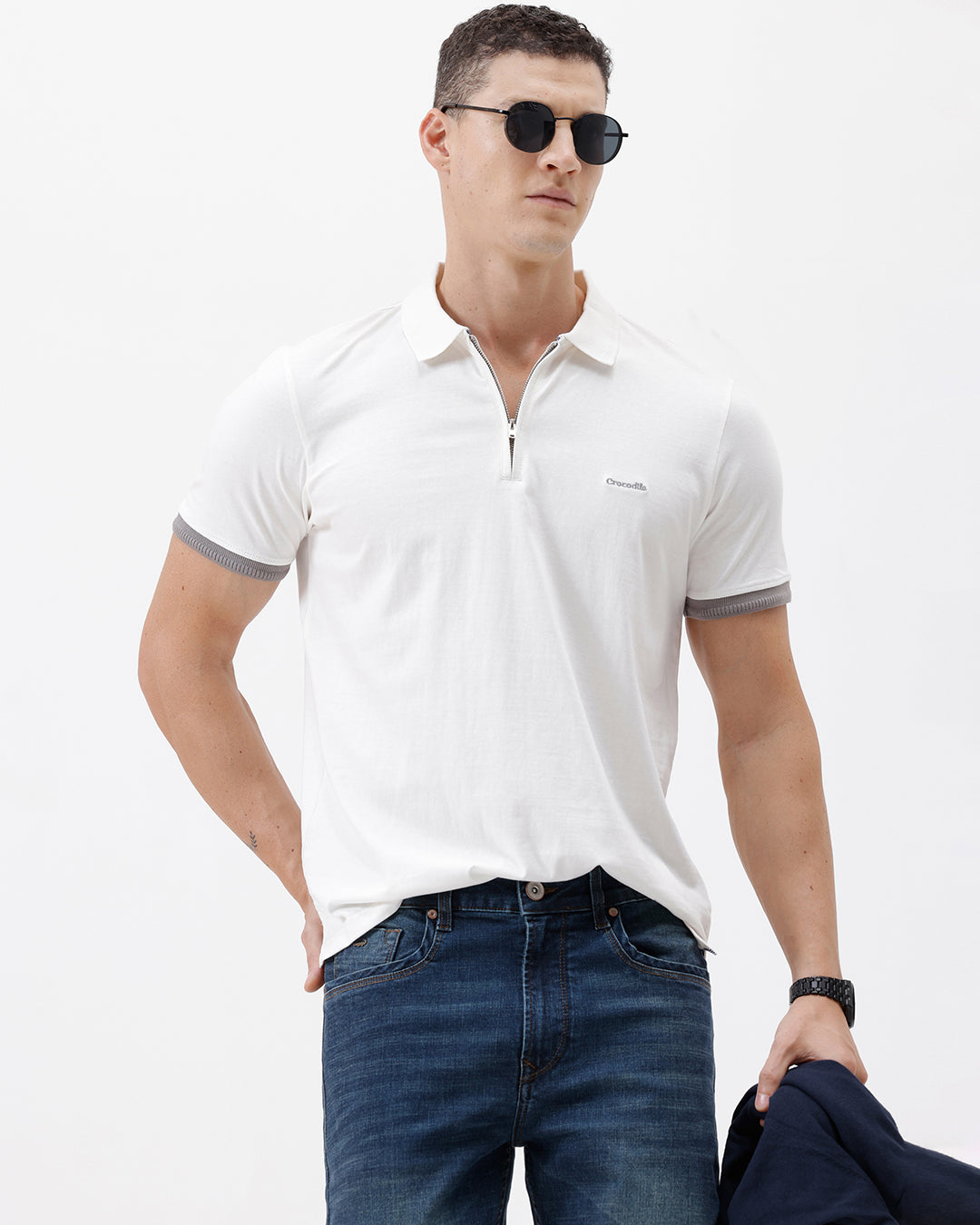A man wearing a white short-sleeve polo shirt with gray ribbed trim on the collar and sleeve cuffs, paired with dark blue jeans, photographed against a plain white studio background.