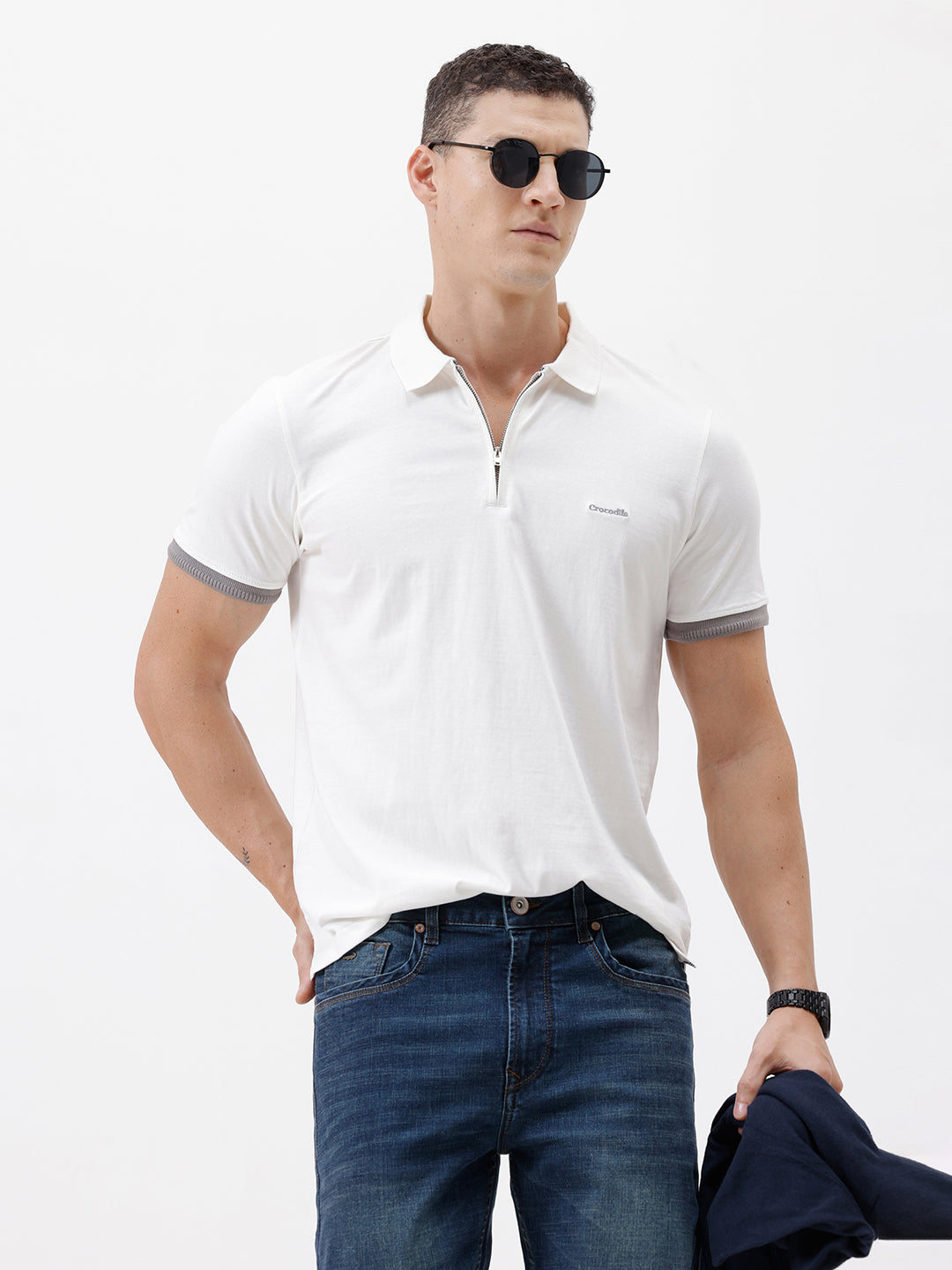 A man wearing a white short-sleeve polo shirt with gray ribbed trim on the collar and sleeve cuffs, paired with dark blue jeans, photographed against a plain white studio background.