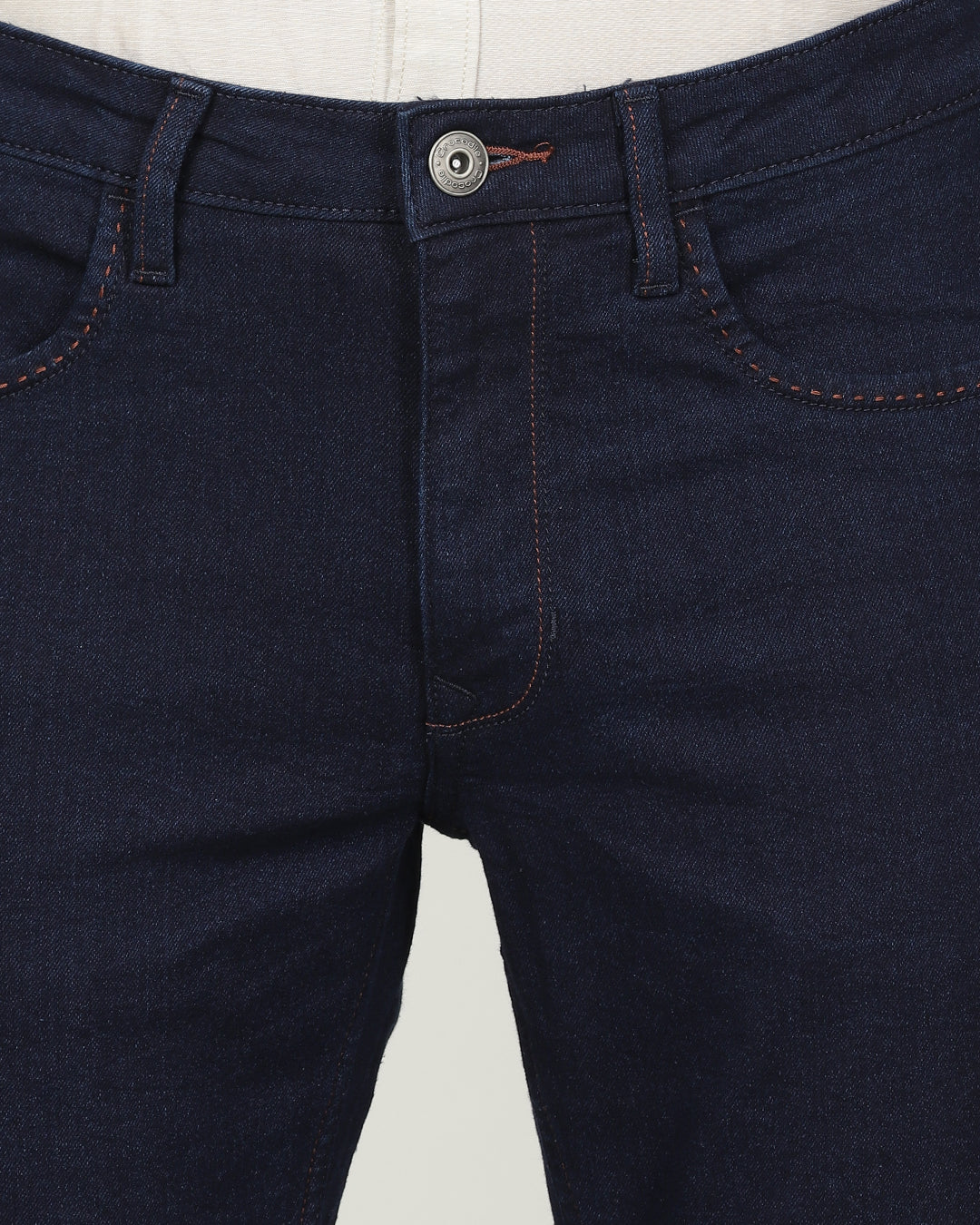 Man wearing a blue dark blue solid mid rise slim tapered jean on a light gray background