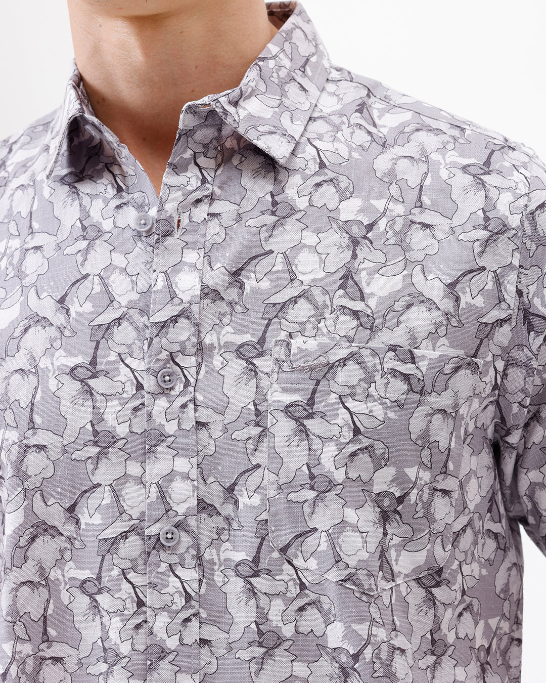 A man wearing a short-sleeve button-up shirt with a gray and white abstract pattern, paired with dark gray trousers, standing against a plain white studio background.