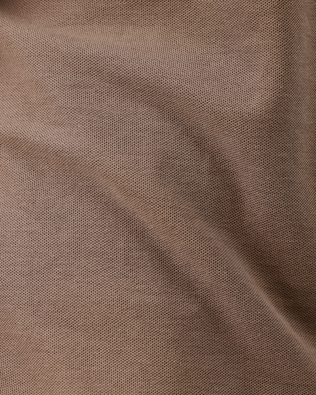A man wearing a brown short-sleeve polo shirt with dark navy pants, standing against a plain light gray studio background.