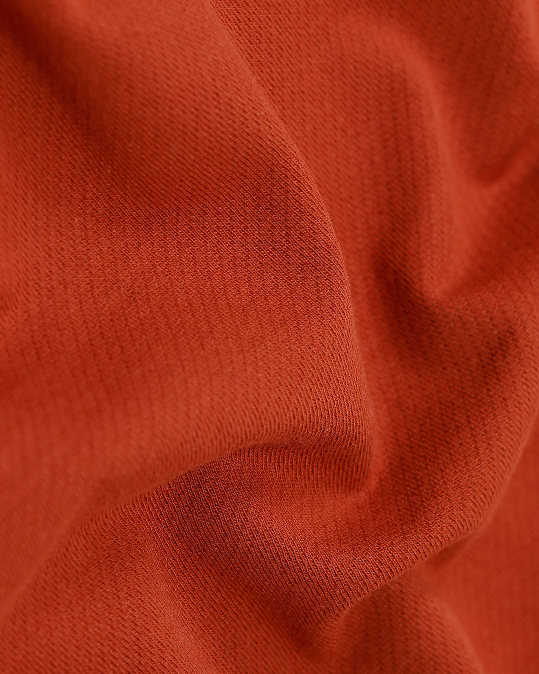 A man wearing a rust-orange short-sleeve polo shirt with a chest pocket, paired with beige cargo pants, standing against a plain light gray studio background.