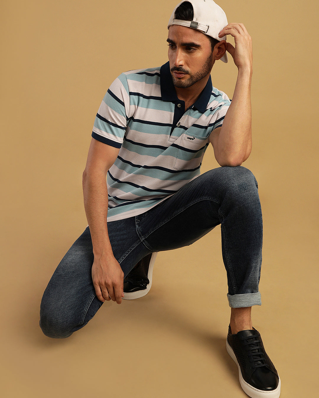 Man wearing a white blue and white striped polo t shirt with casual styling on a gray background