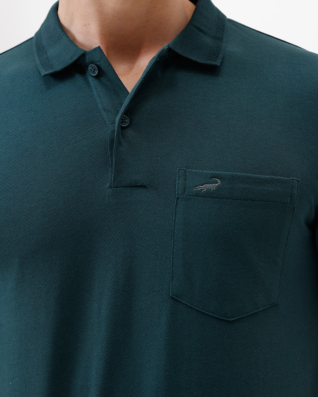 A man wearing a dark teal short-sleeve polo shirt with a chest pocket, paired with beige cargo pants, standing against a plain white studio background.