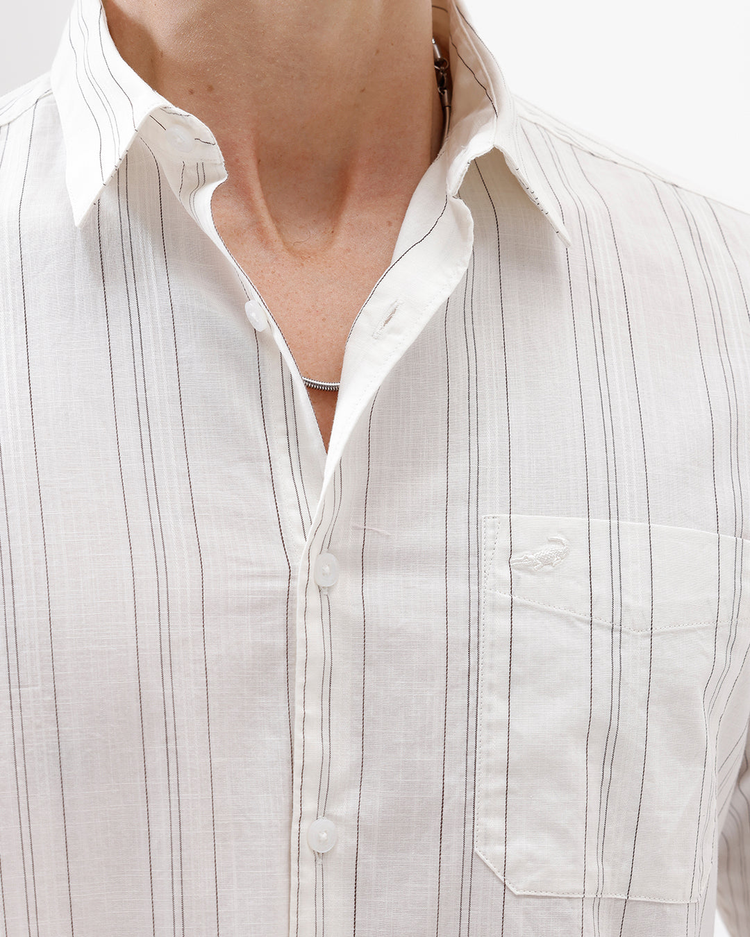 A man wearing a white long-sleeve button-up shirt with thin vertical gray stripes and black pants, standing against a plain white studio background.