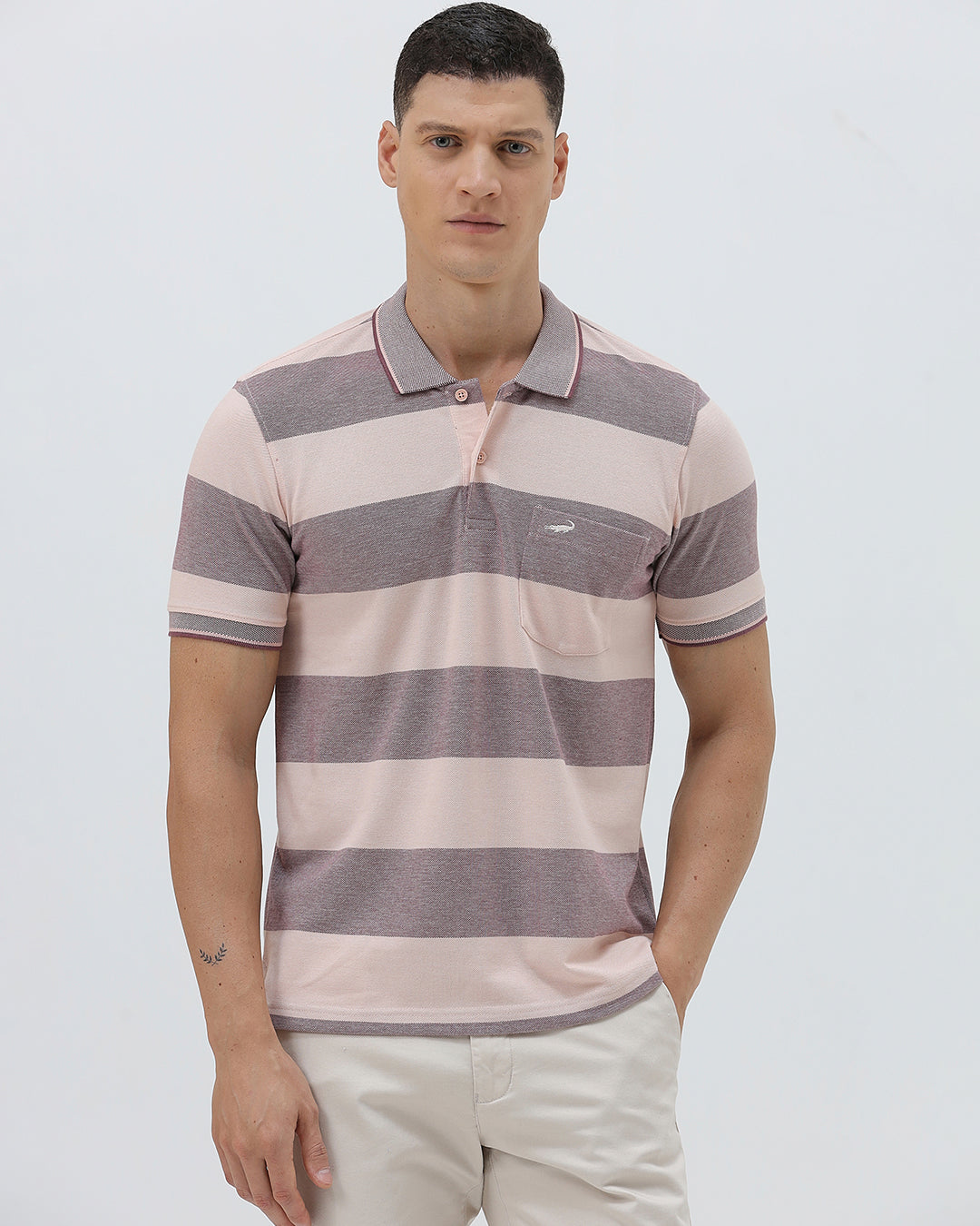 A man wearing a short-sleeve polo shirt with horizontal stripes in dusty pink and gray, paired with light beige trousers, against a plain light gray background.