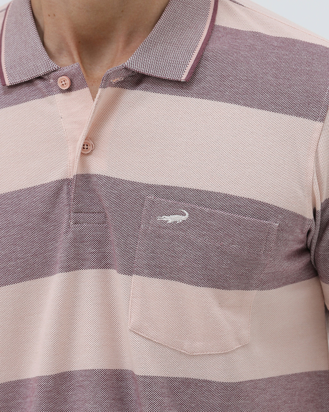A man wearing a short-sleeve polo shirt with horizontal stripes in dusty pink and gray, paired with light beige trousers, against a plain light gray background.