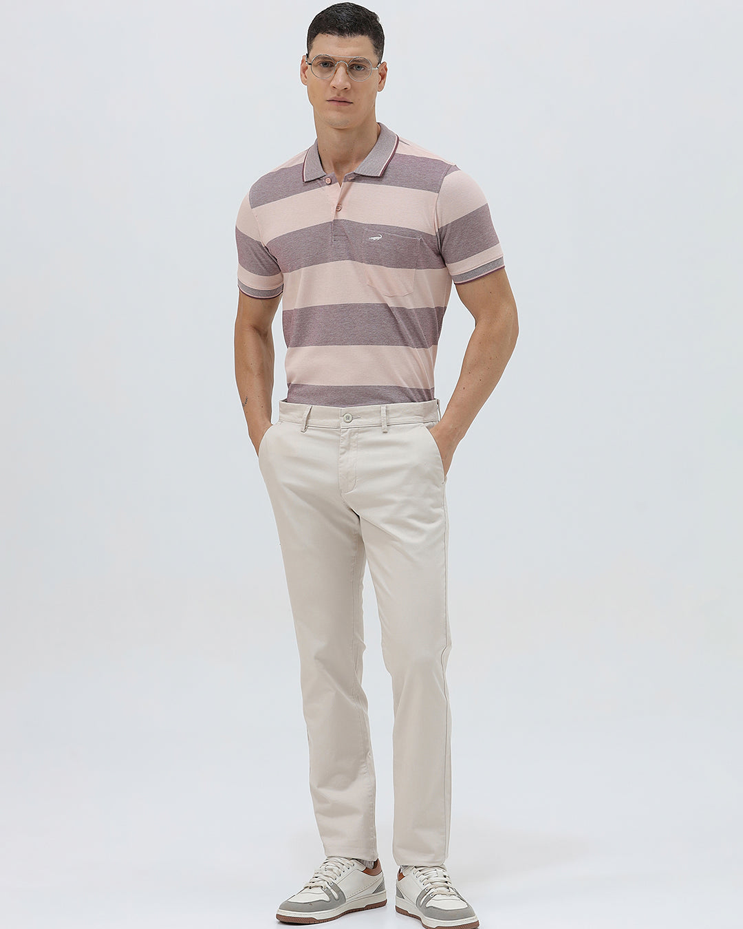 A man wearing a short-sleeve polo shirt with horizontal stripes in dusty pink and gray, paired with light beige trousers, against a plain light gray background.