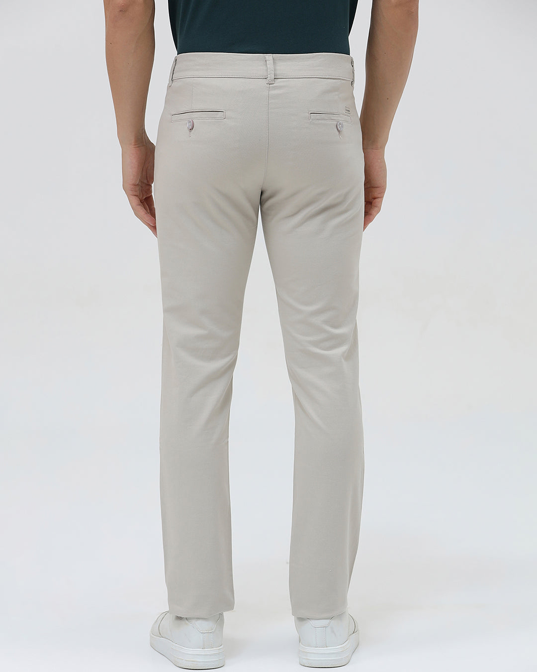 A person wearing slim-fit light beige chinos with a dark green t-shirt and white sneakers, standing against a plain white studio background.