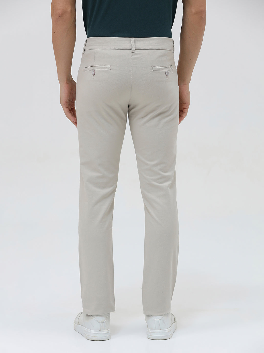 A person wearing slim-fit light beige chinos with a dark green t-shirt and white sneakers, standing against a plain white studio background.