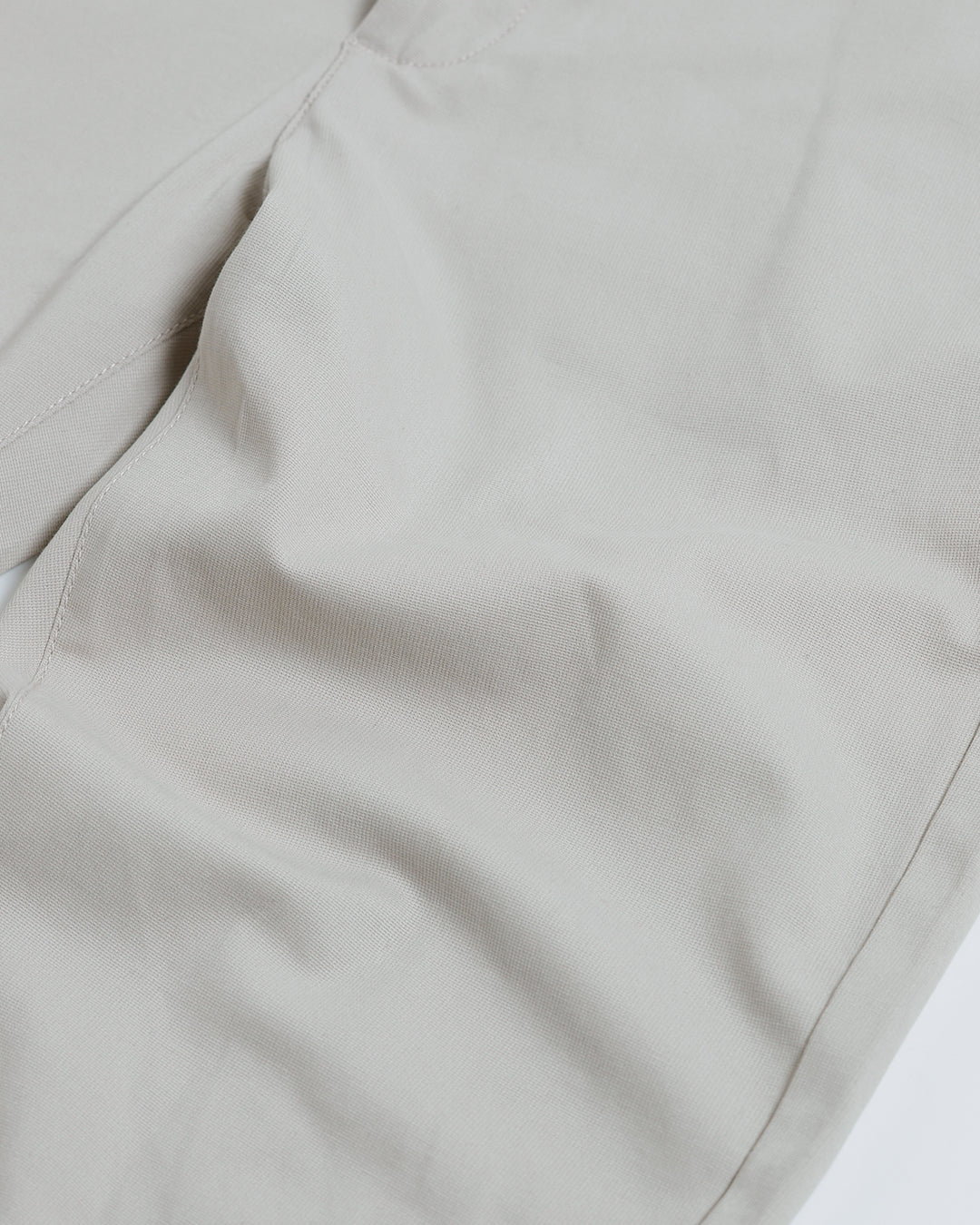 A person wearing slim-fit light beige chinos with a dark green t-shirt and white sneakers, standing against a plain white studio background.