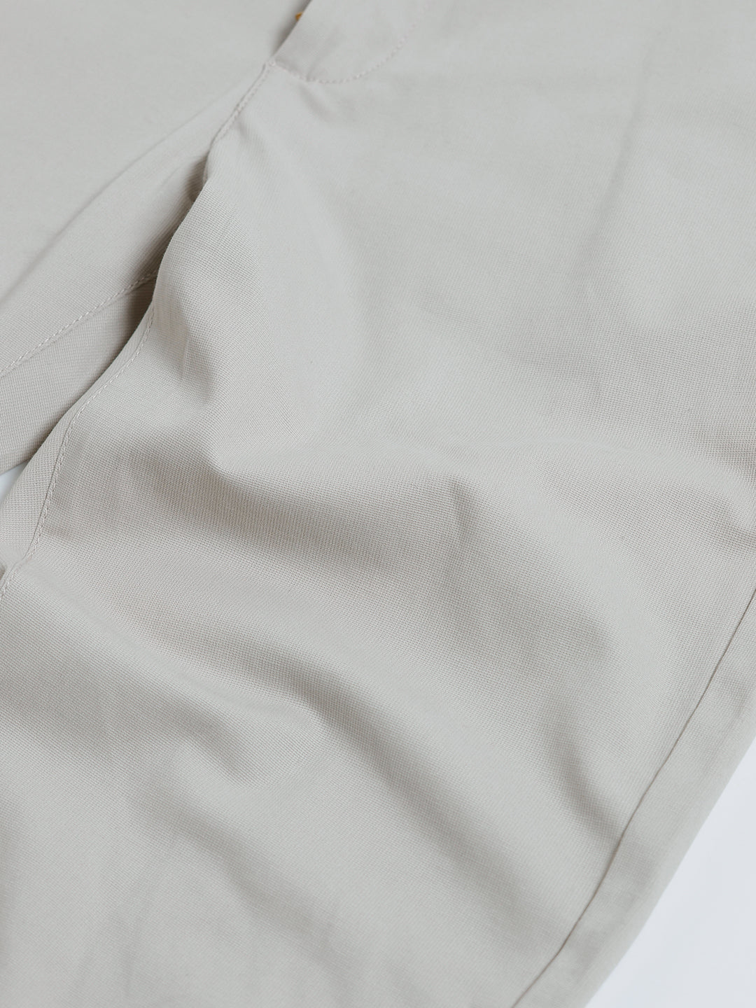 A person wearing slim-fit light beige chinos with a dark green t-shirt and white sneakers, standing against a plain white studio background.