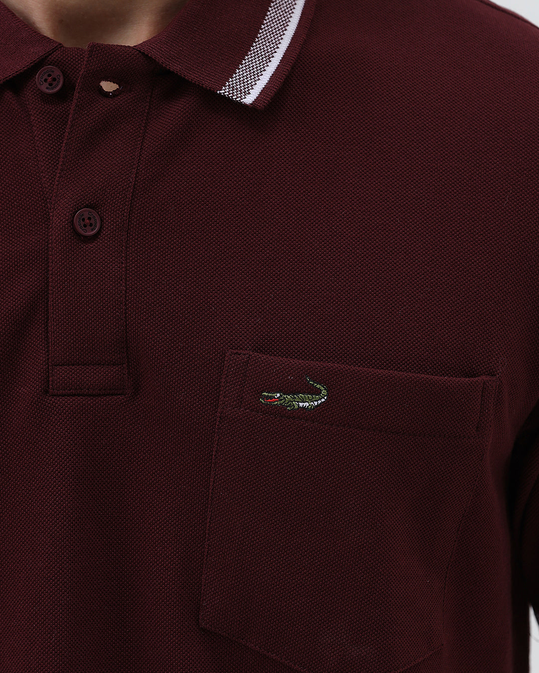 A man wearing a short-sleeve polo shirt in maroon with a contrasting light gray and white striped collar and sleeve cuffs, paired with light gray cargo pants, against a plain light gray background.