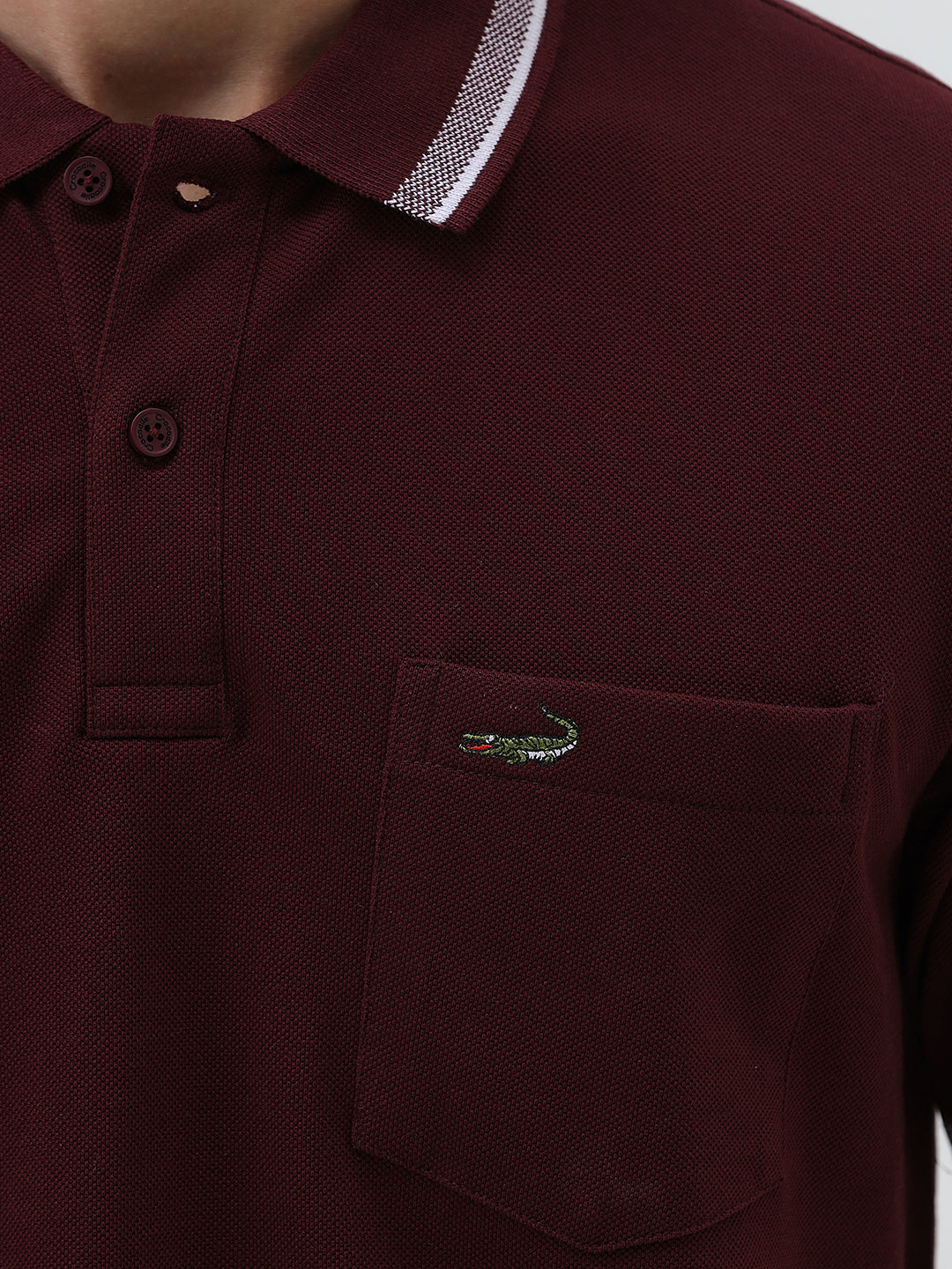 A man wearing a short-sleeve polo shirt in maroon with a contrasting light gray and white striped collar and sleeve cuffs, paired with light gray cargo pants, against a plain light gray background.