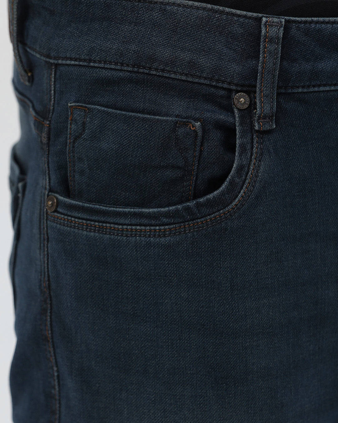 A person wearing dark blue slim-fit denim jeans, paired with a black t-shirt and navy and white sneakers, standing against a plain white studio background.