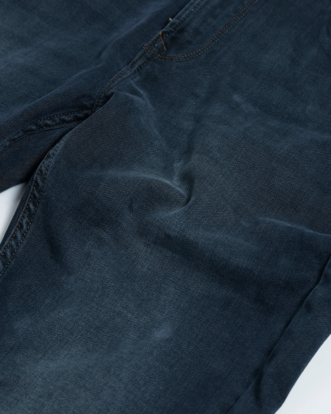 A person wearing dark blue slim-fit denim jeans, paired with a black t-shirt and navy and white sneakers, standing against a plain white studio background.