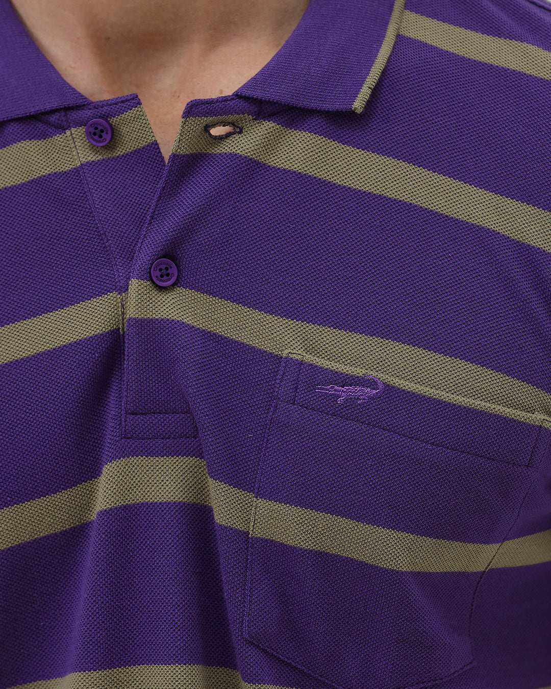 A man wearing a purple short-sleeve polo shirt with horizontal olive green stripes, paired with dark gray pants, standing against a light gray studio background.