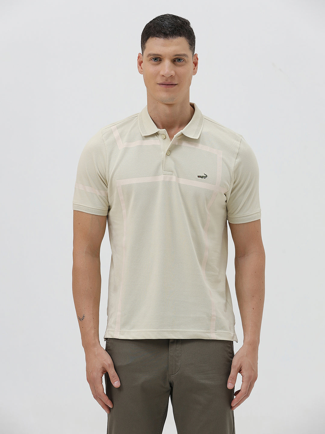 A man wearing a light beige short-sleeve polo shirt with subtle horizontal stripe details and a small crocodile logo on the left chest, paired with olive green trousers, against a plain light gray background.