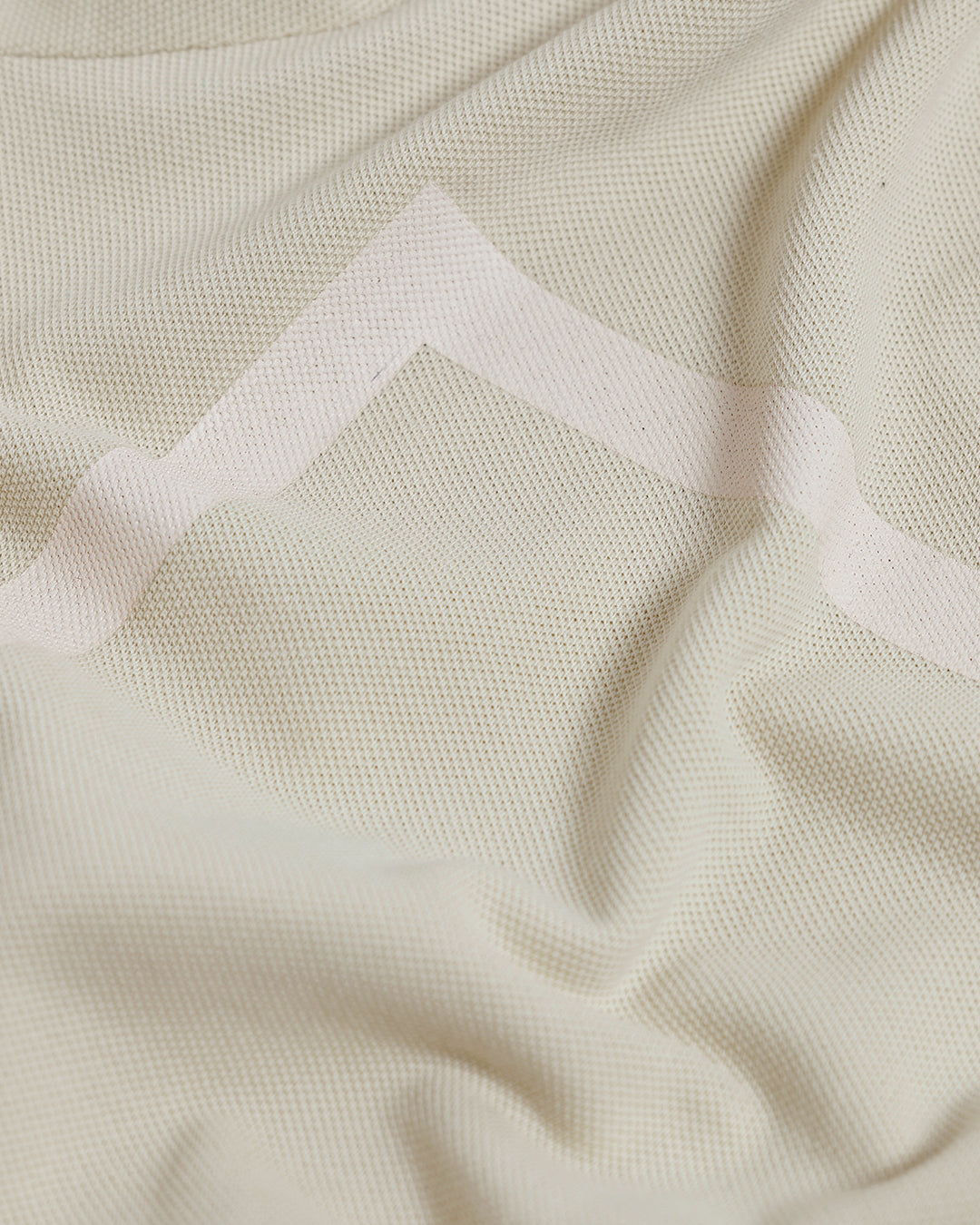 A man wearing a light beige short-sleeve polo shirt with subtle horizontal stripe details and a small crocodile logo on the left chest, paired with olive green trousers, against a plain light gray background.