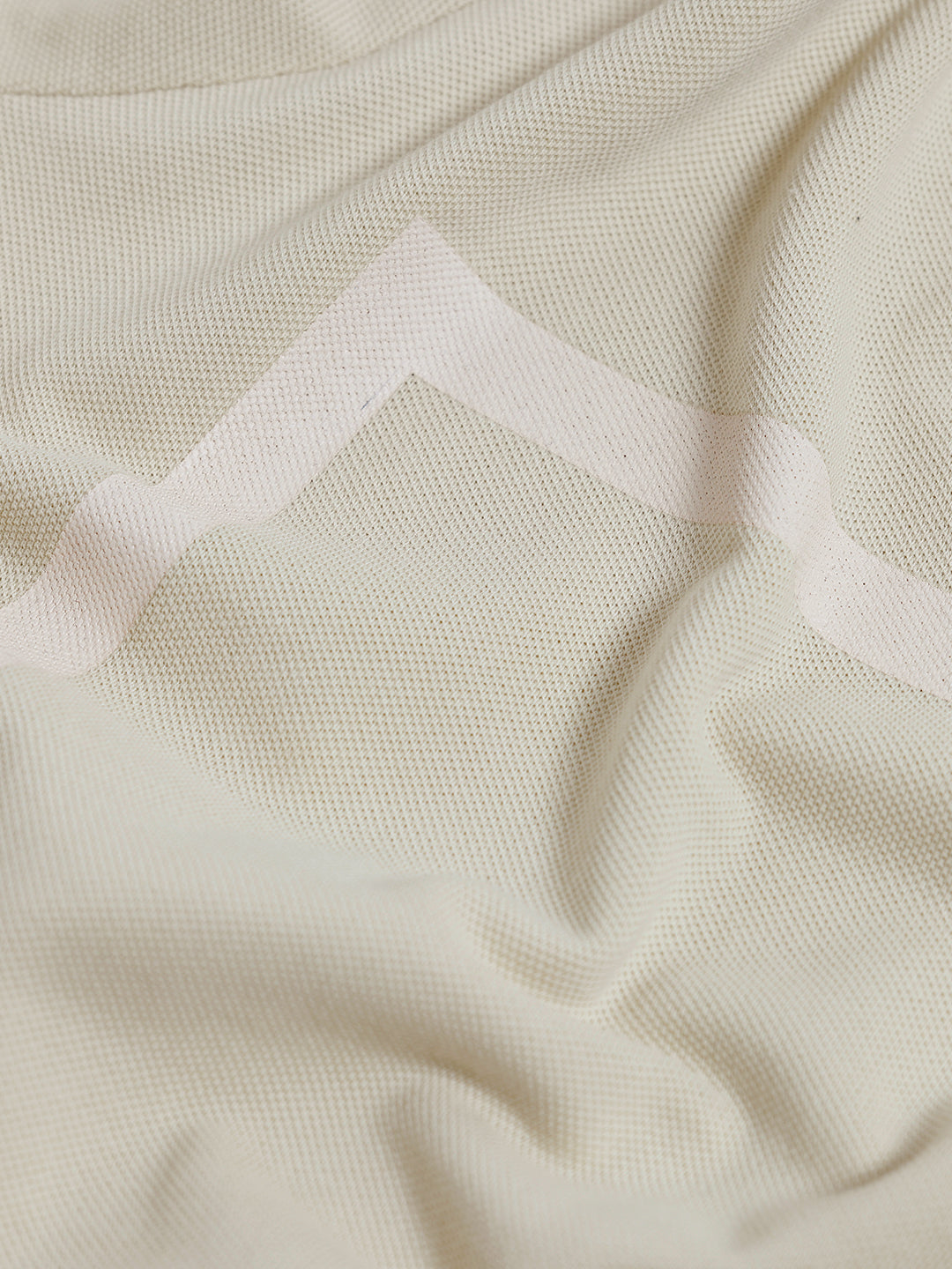 A man wearing a light beige short-sleeve polo shirt with subtle horizontal stripe details and a small crocodile logo on the left chest, paired with olive green trousers, against a plain light gray background.