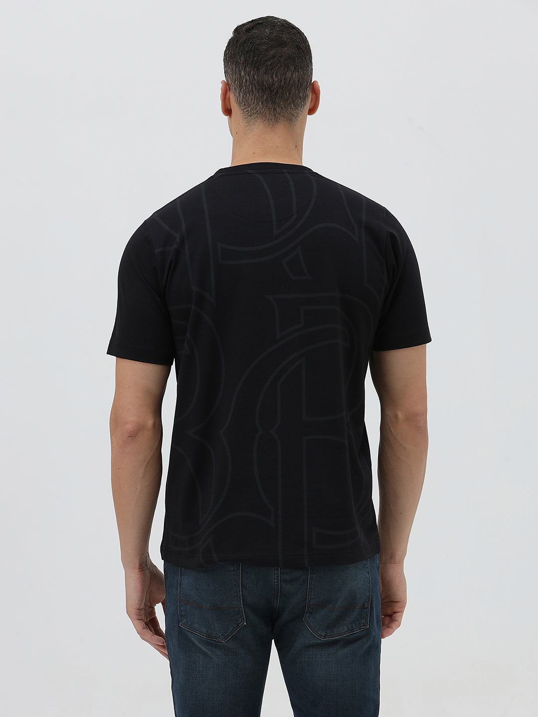 A man wearing a black short-sleeve t-shirt with a subtle tonal geometric pattern and a small 'Gildan' logo on the left chest, paired with dark blue jeans, against a light gray studio background.