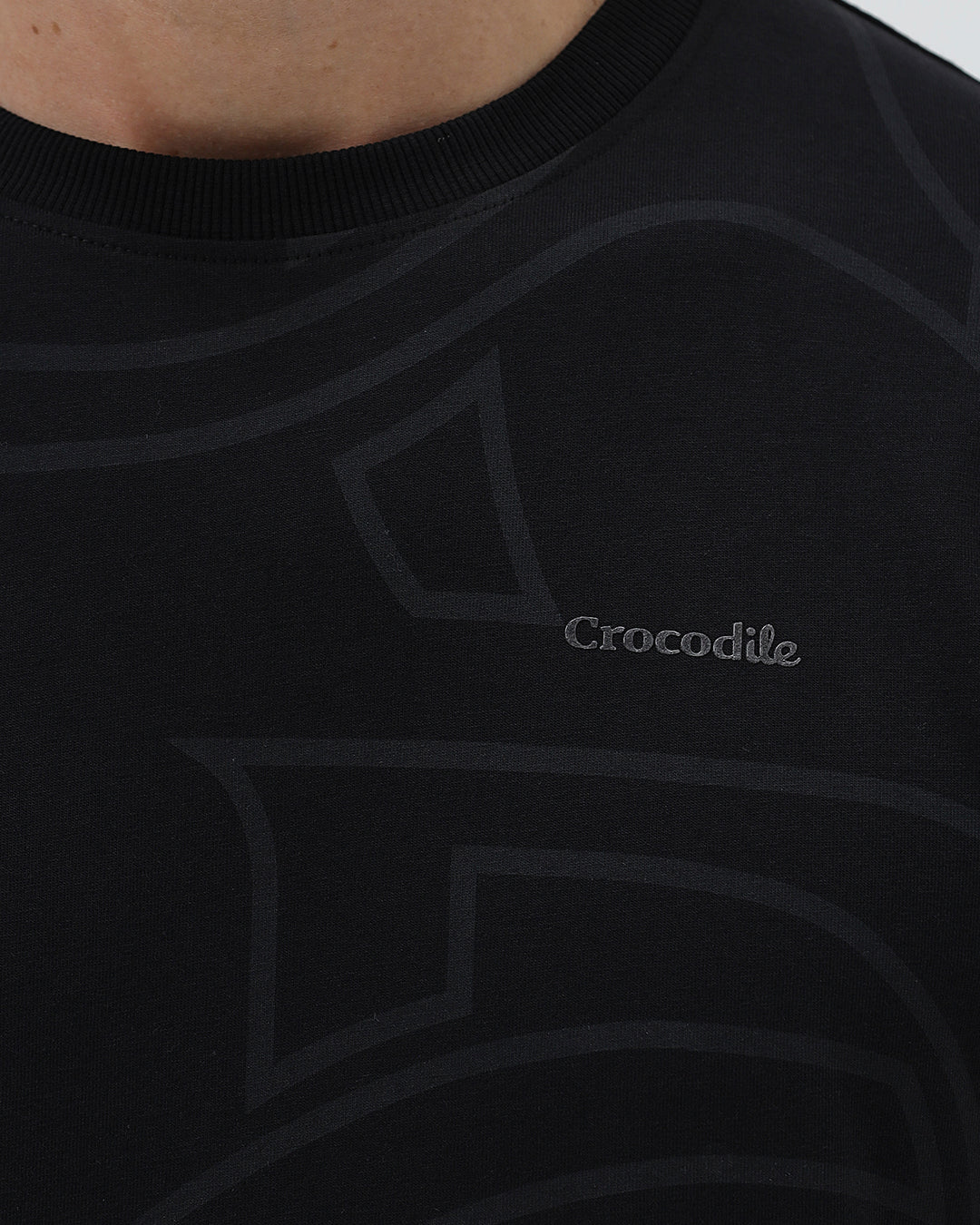 A man wearing a black short-sleeve t-shirt with a subtle tonal geometric pattern and a small 'Gildan' logo on the left chest, paired with dark blue jeans, against a light gray studio background.