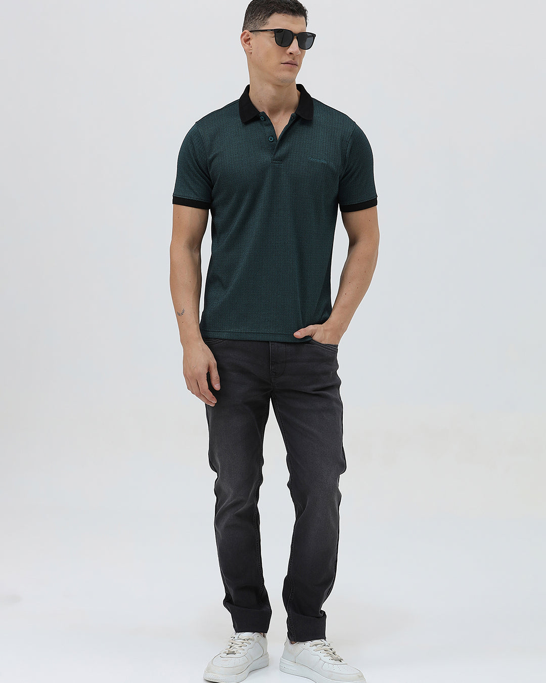 A person wearing slim-fit black denim jeans with a dark green top and white sneakers, shown from the waist down against a plain light gray studio background.