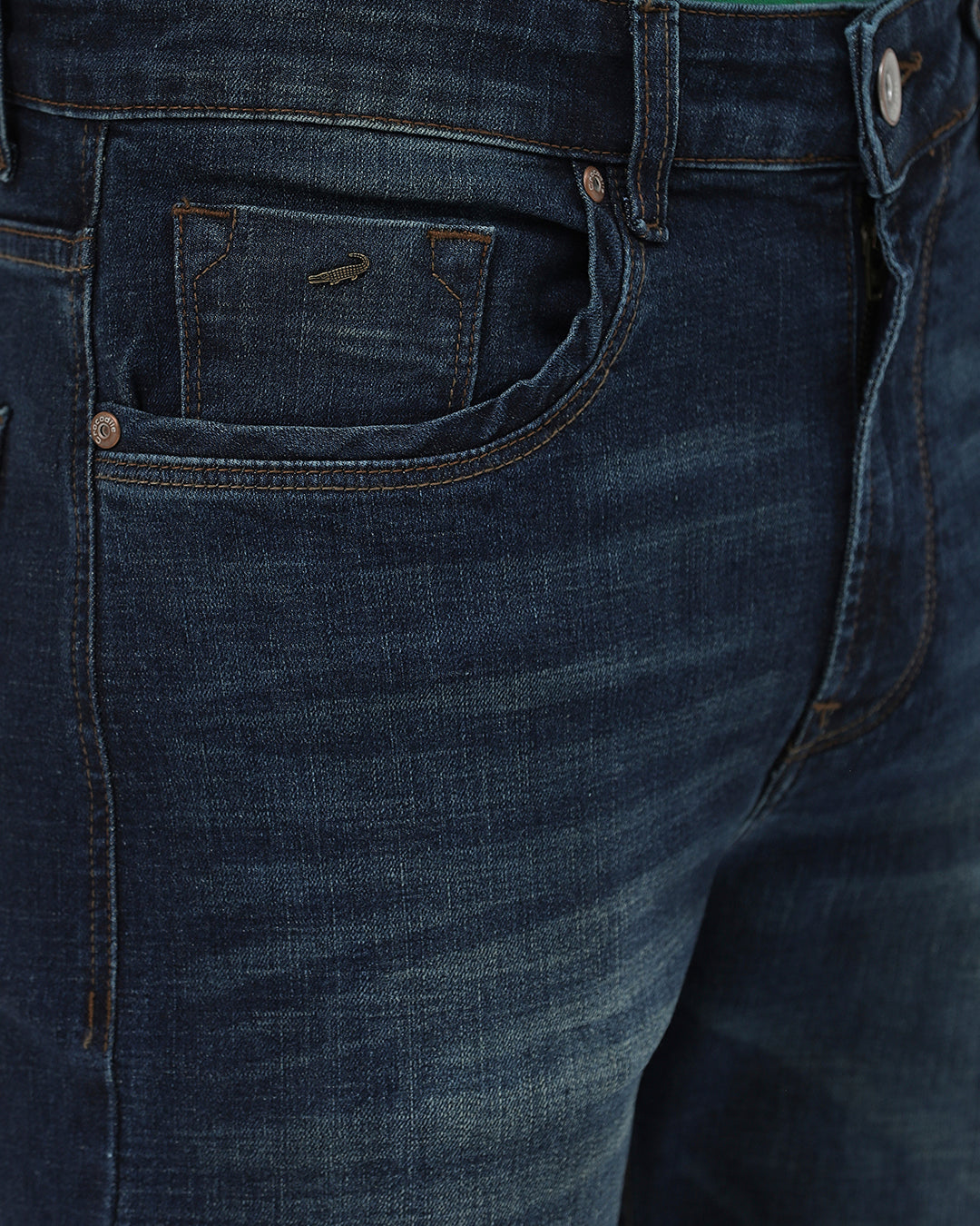 A person wearing dark blue slim-fit jeans, a green shirt, and navy and white sneakers, standing against a light gray studio background.